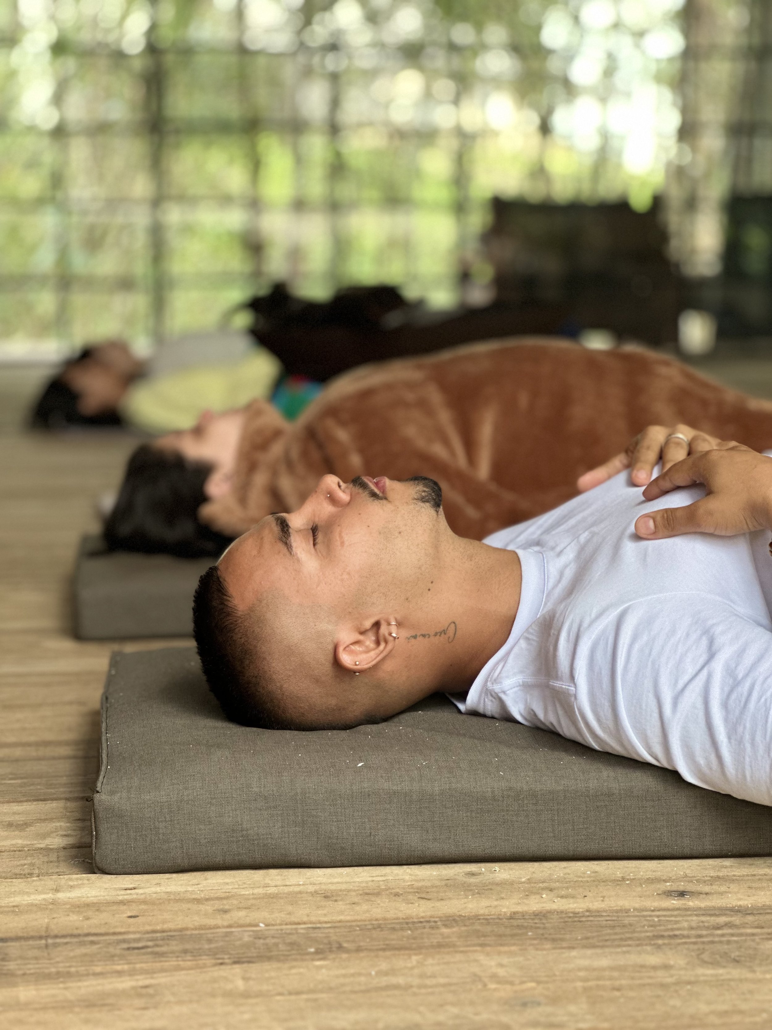 Personas recostadas en tapetes en un ambiente natural, participando en una actividad de relajación o meditación guiada por Manuel Marín
