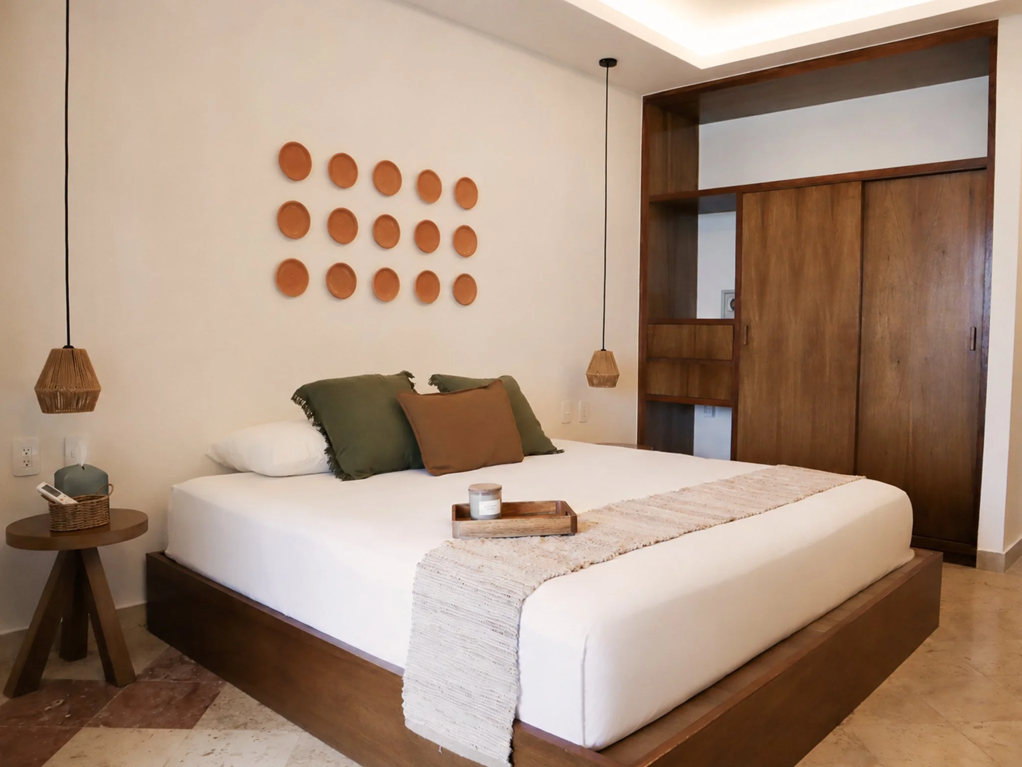 A cozy bedroom featuring a wooden bed with white bedding and decorative pillows, two bedside tables, and pendant lights hanging from the ceiling.