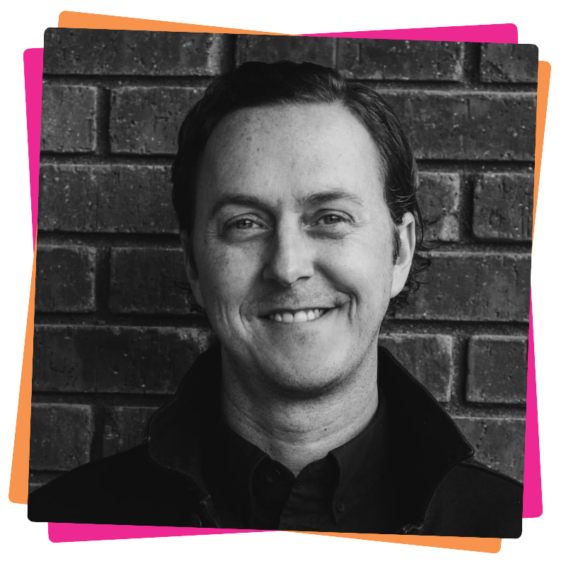 Headshot of Ryan Rumsey. He stands against a brick wall and smiles. 