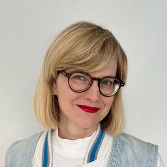 Headshot of Hertje Brodersen. She has blond hair and wears glasses and red lipstick.