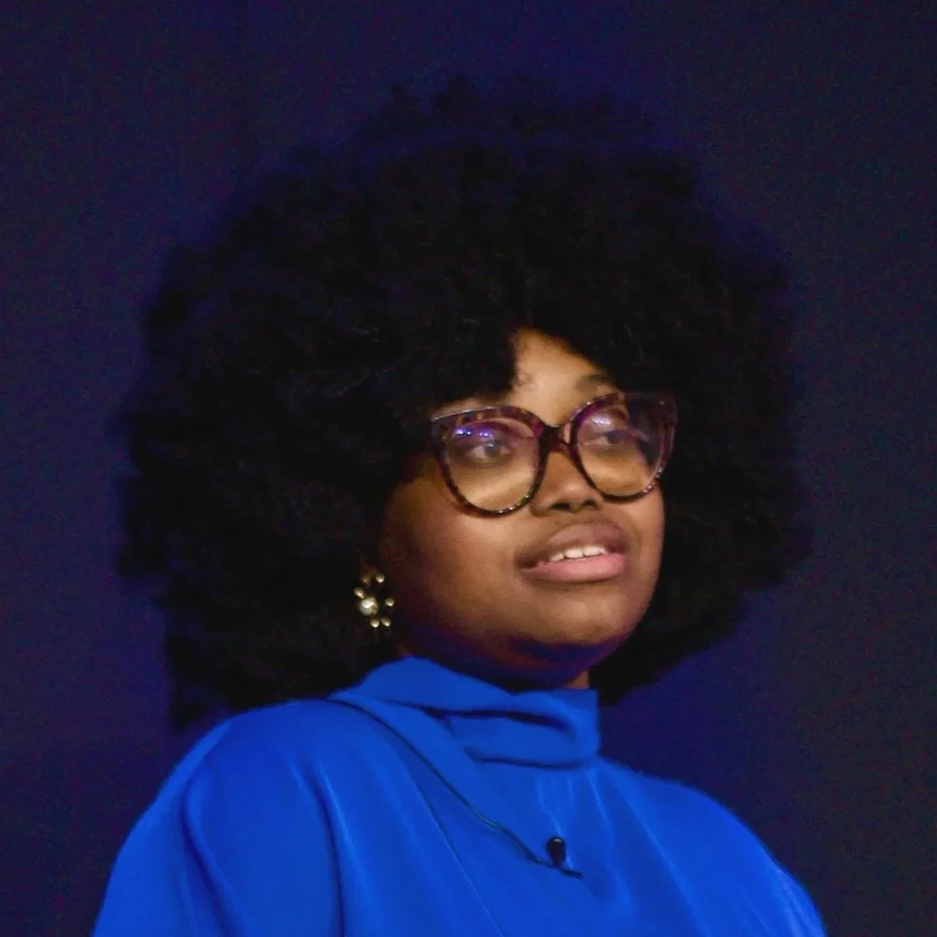 Headshot of Ìníolúwa Abíódún, a Black woman wearing a blue top and glasses with curly hair.