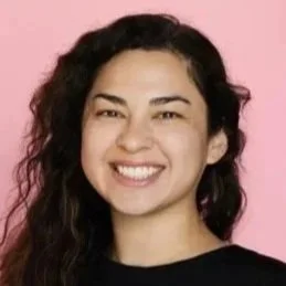 Headshot of Desirée García, a Latina woman with dark, wavy hair wearing a black top. She stands against a pink background.