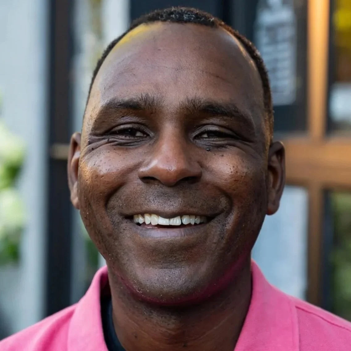 Headshot of Ron Bronson, a Black man in a pink collared shirt smiling.