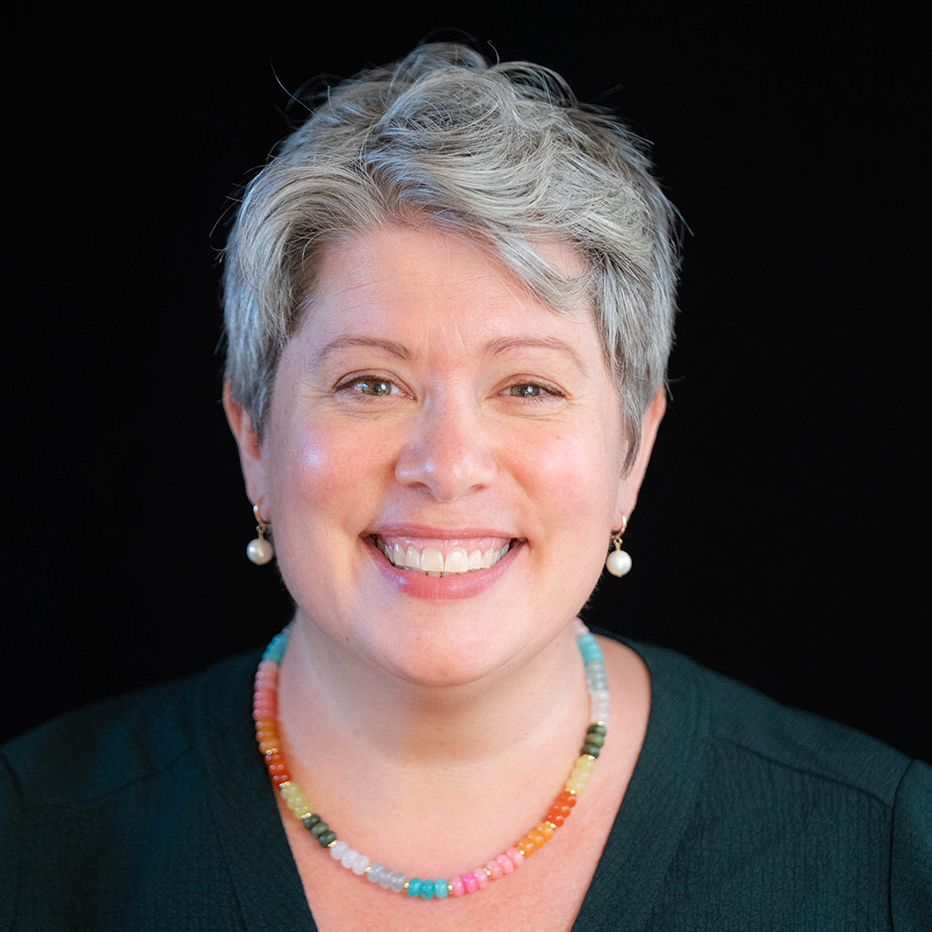 Headshot of Torrey Podmajersky. They have short gray hair and wear a teal top and colorful necklace.