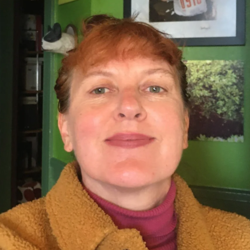 Headshot of Erika Hall, a person with red hair, a maroon turtleneck, and a camel-colored coat.