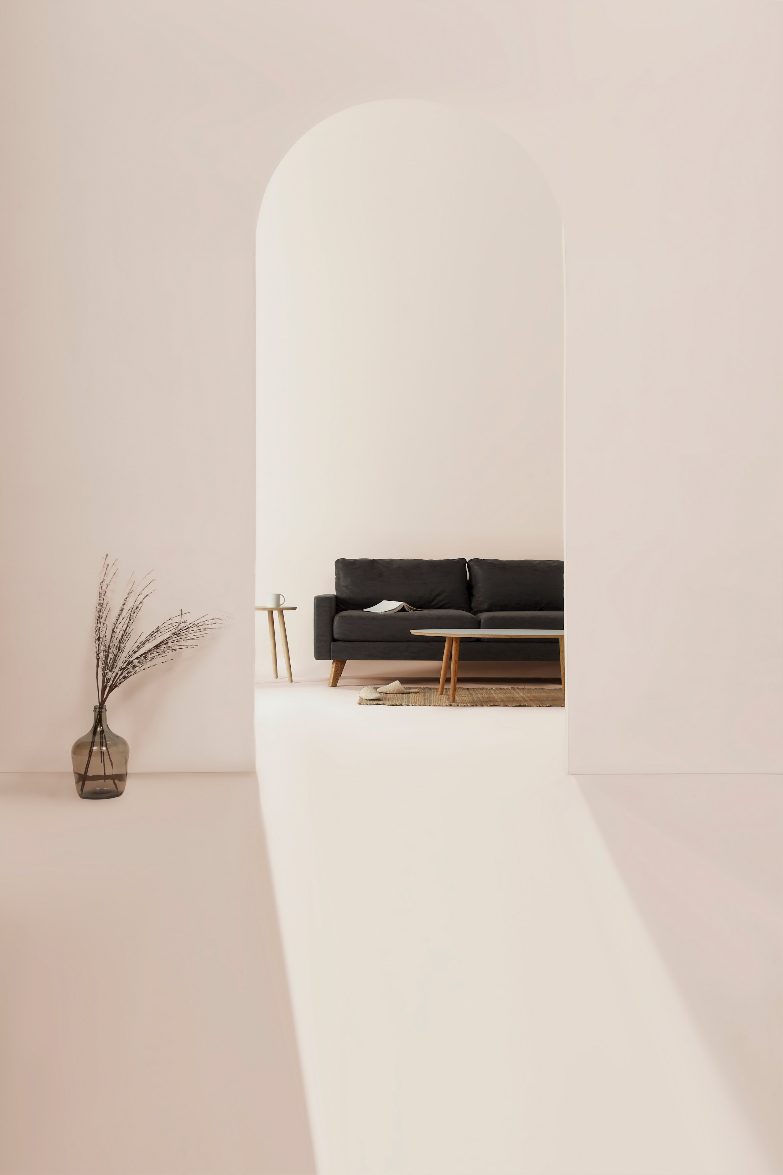 Minimalist living room viewed through an arched doorway with a black sofa, a small wooden side table, a coffee table, and a vase with dried grasses.