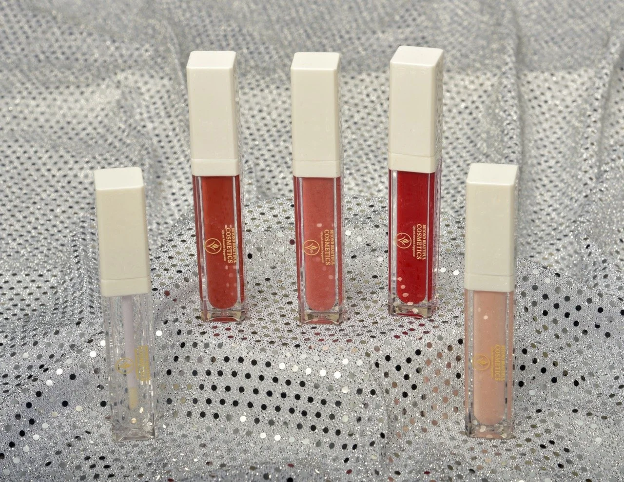 Five tubes of liquid cosmetics in various shades, standing upright on a sparkly surface with a silver background.
