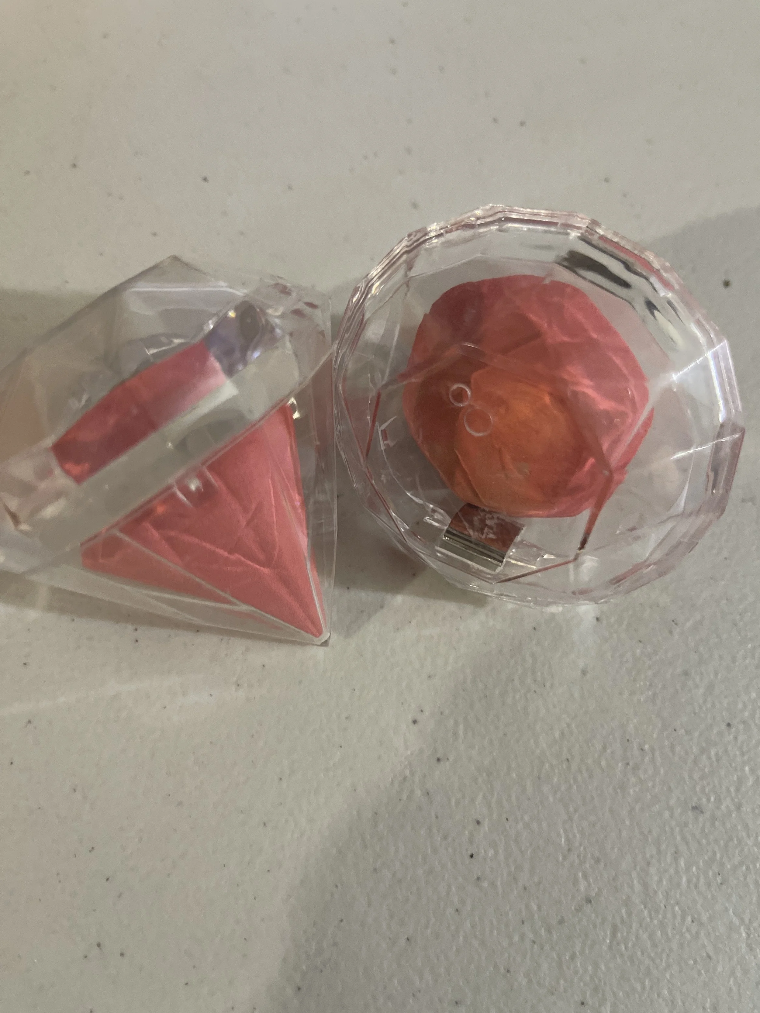 Two clear plastic containers with pink and red wrapped items inside, one standing upright and the other lying on its side. Beyond Beautiful Cosmetics Gifts and Interactive Engagements 