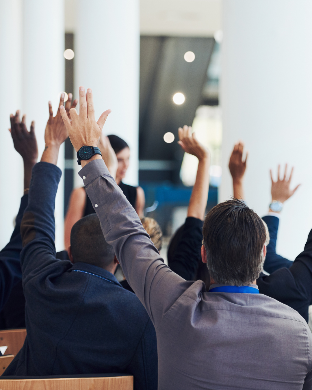 Multiple people in a conference room raising their hands during a meeting or presentation.