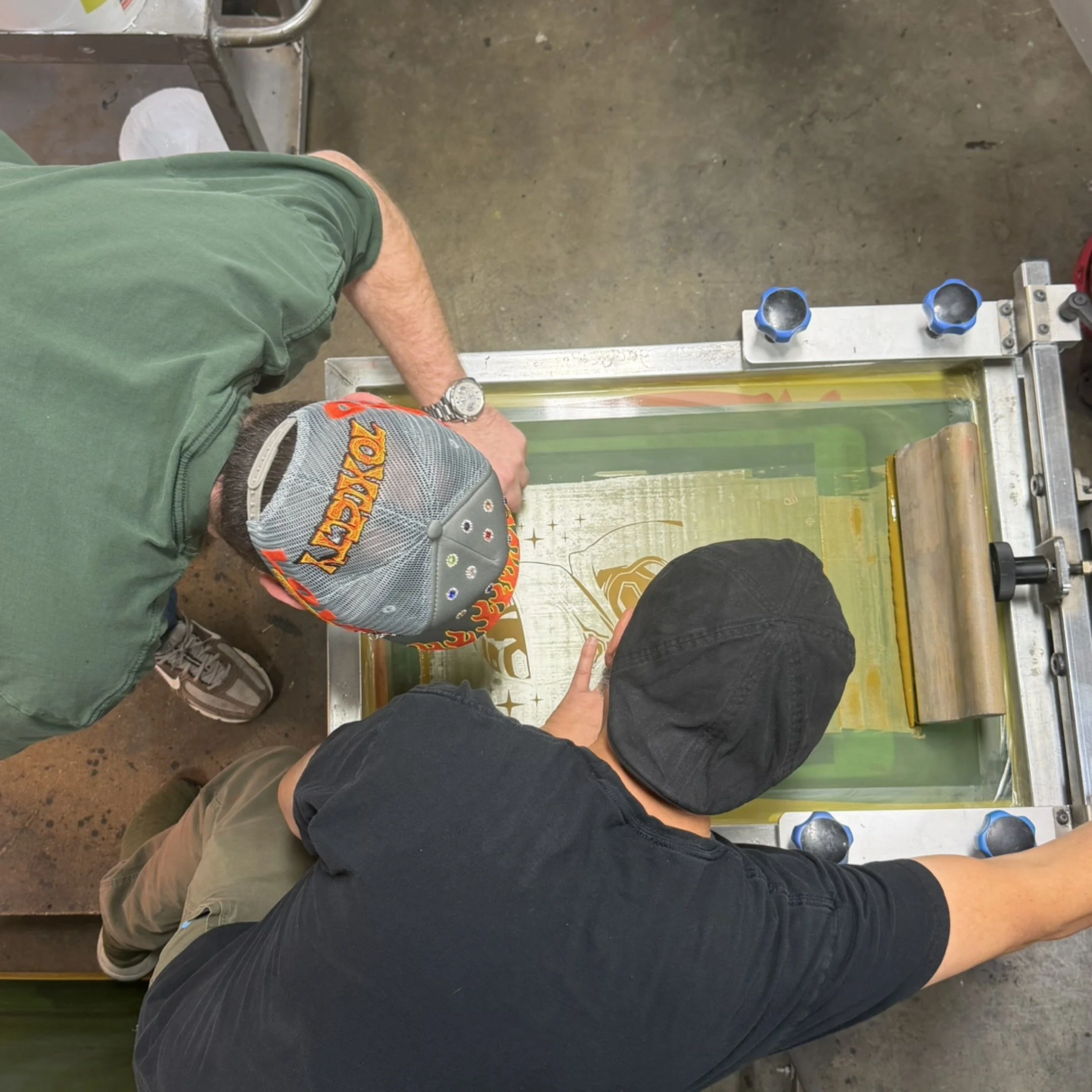 Two boys are working on a screen printing press, creating a design on a piece of fabric or paper.