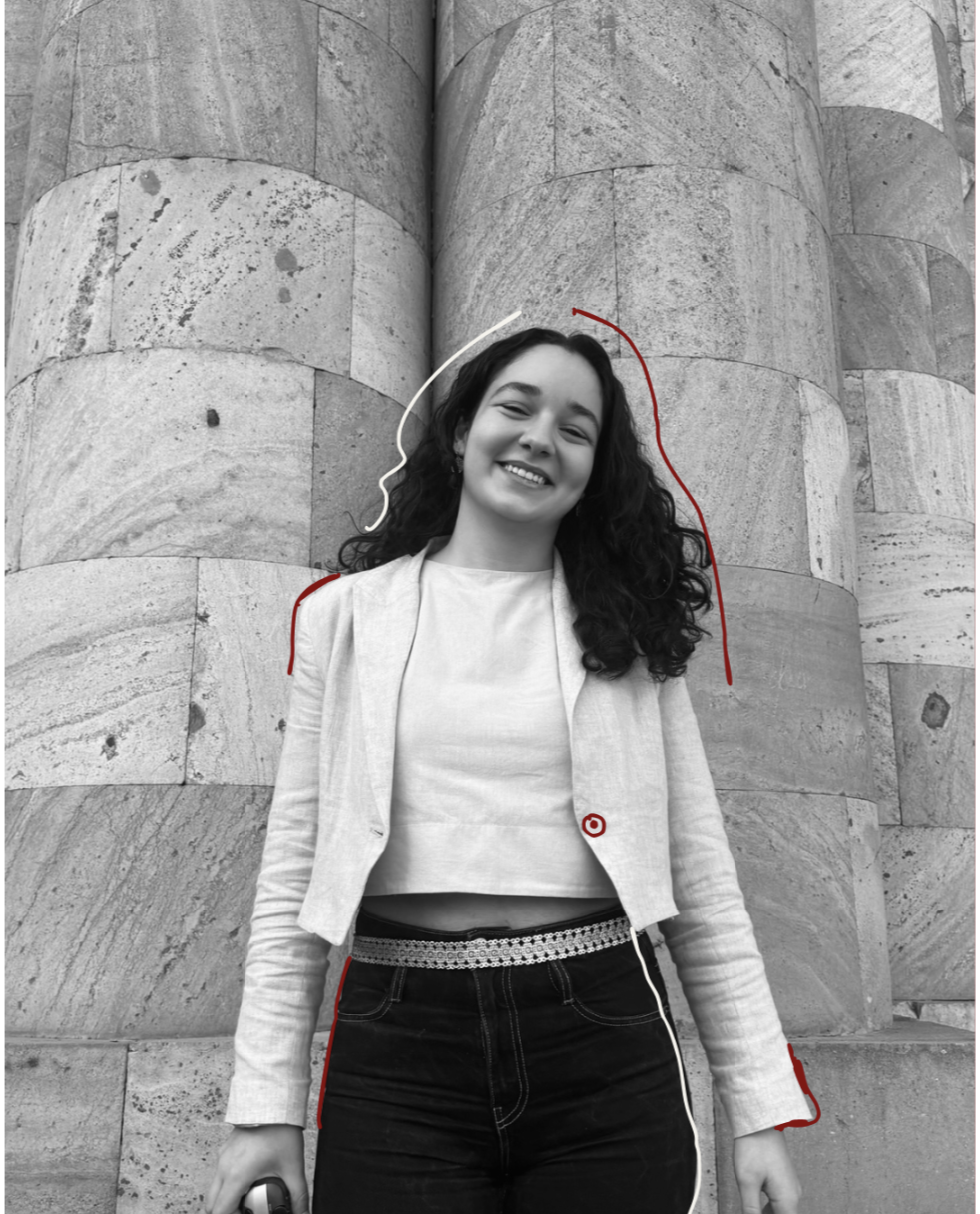 A smiling young woman with curly hair standing in front of a stone wall. The photo is in black and white with some red and white lines drawn on her hair and body.