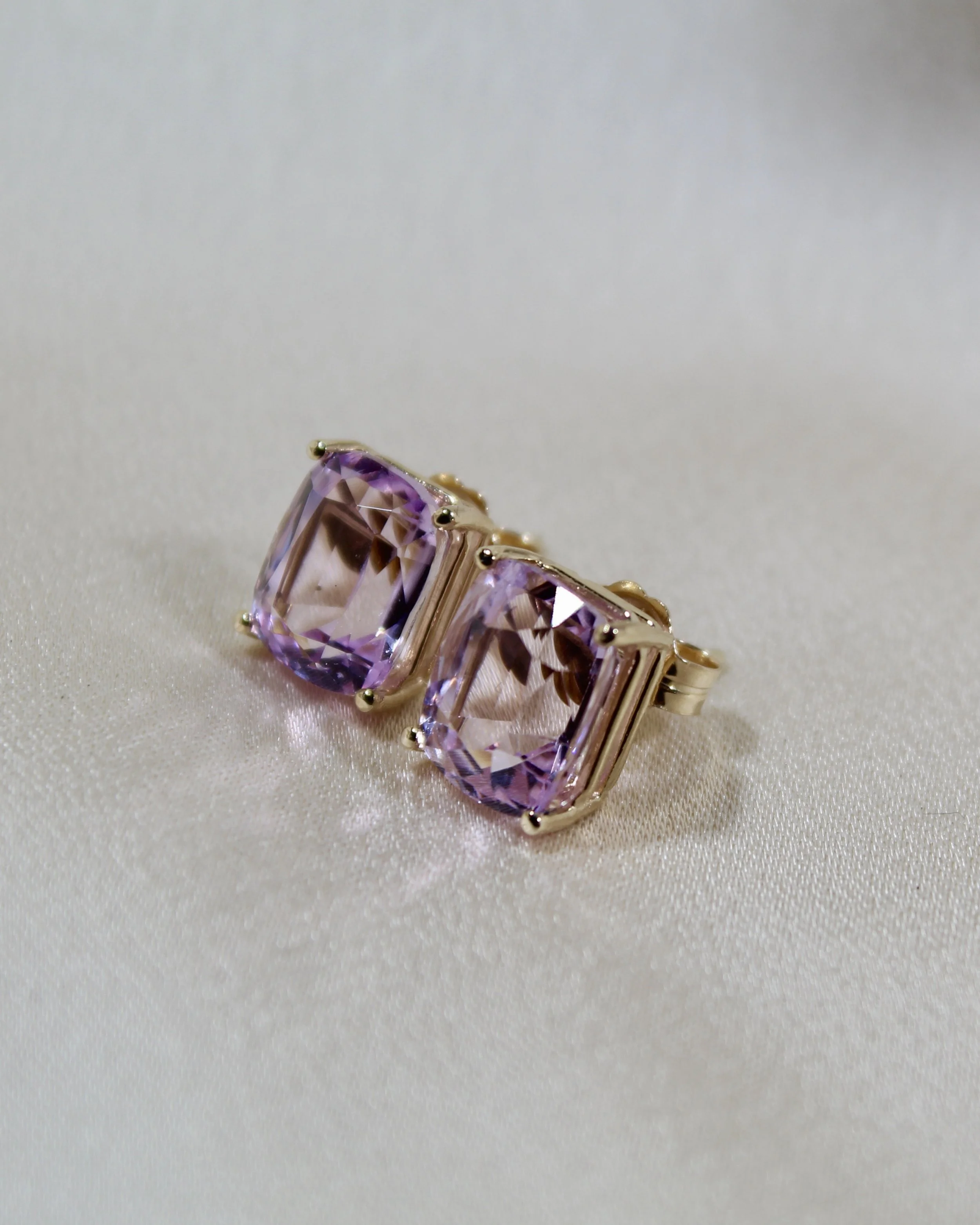 A gold ring with two large, rectangular purple gemstones setting on a satin surface.