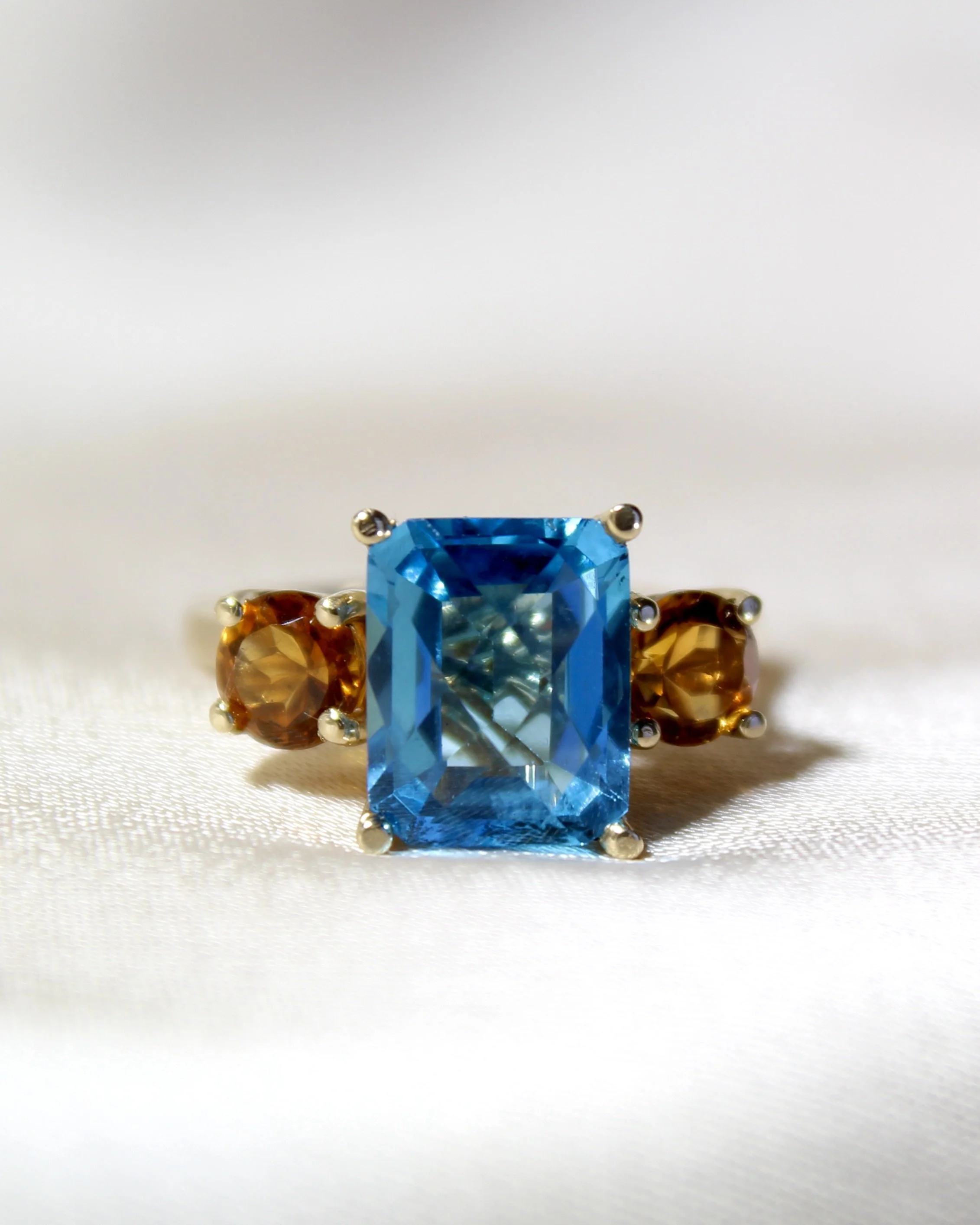 Ring with a large rectangular blue gemstone flanked by two smaller round orange gemstones.