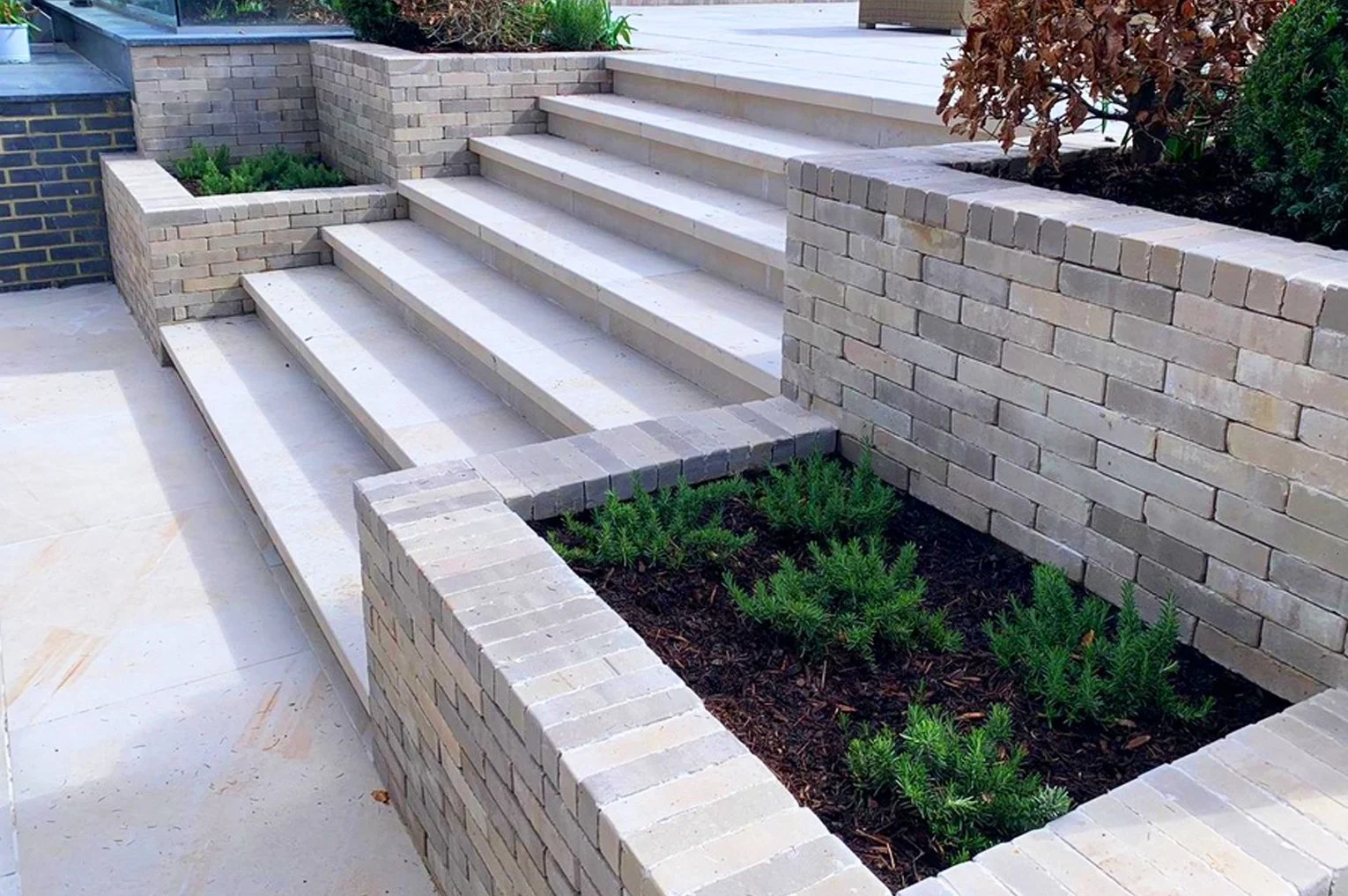 Contemporary garden design with wide stone steps and integrated brick planters filled with greenery, showcasing a modern landscaped terrace.
