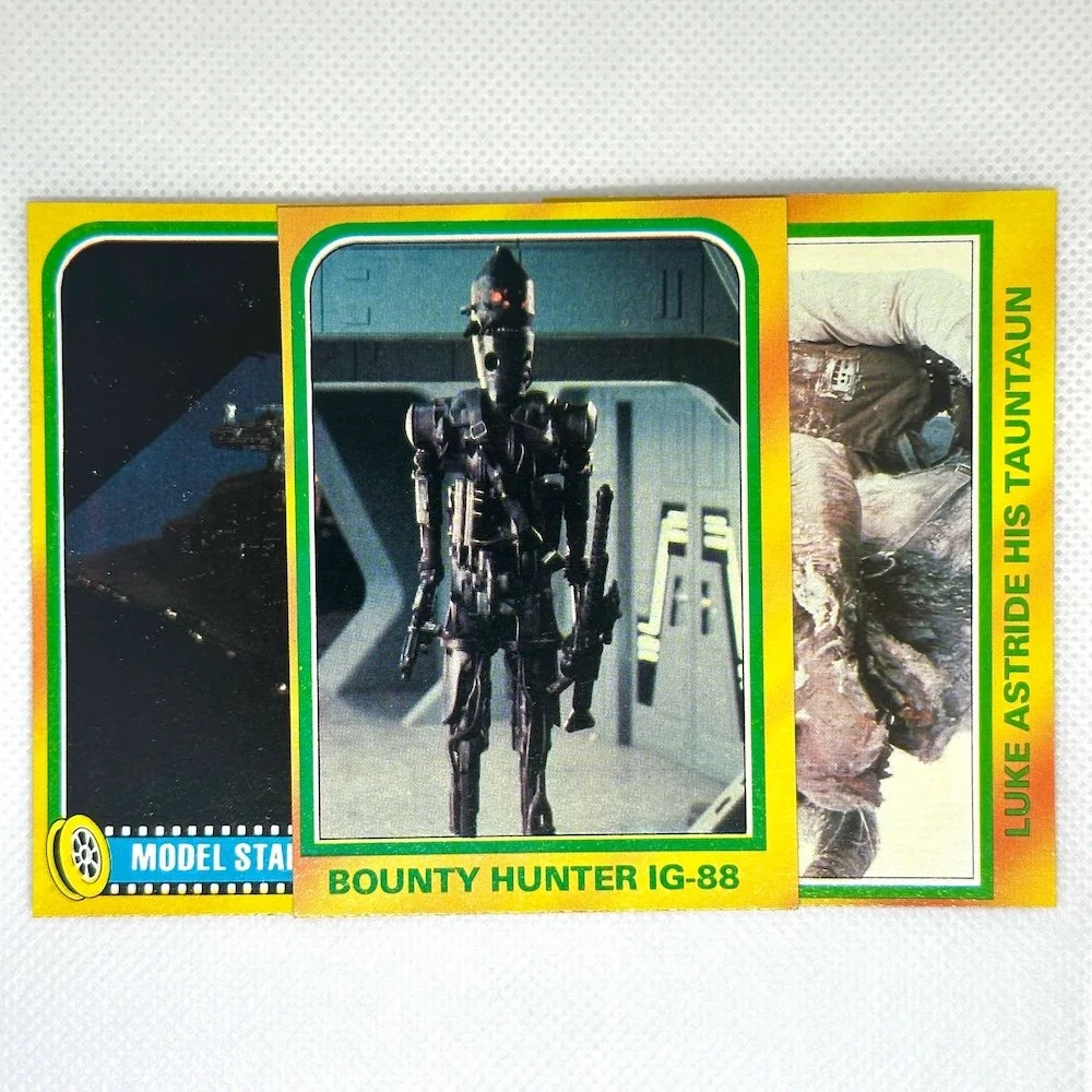 Three vintage Star Wars trading cards featuring scenes from the original trilogy on a white background. The middle card shows a Bounty Hunter IG-88, the right card depicts Luke Skywalker fighting a Tauntaun, and the left card is partially visible.