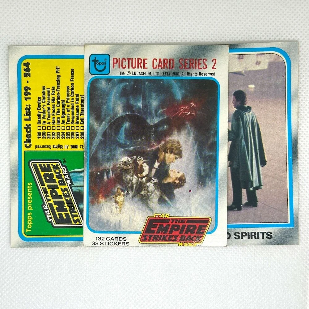 Collection of vintage Star Wars trading cards, including a Topps Star Wars Empire Strikes Back series card with Darth Vader, and another card showing a person in a coat walking in a corridor.