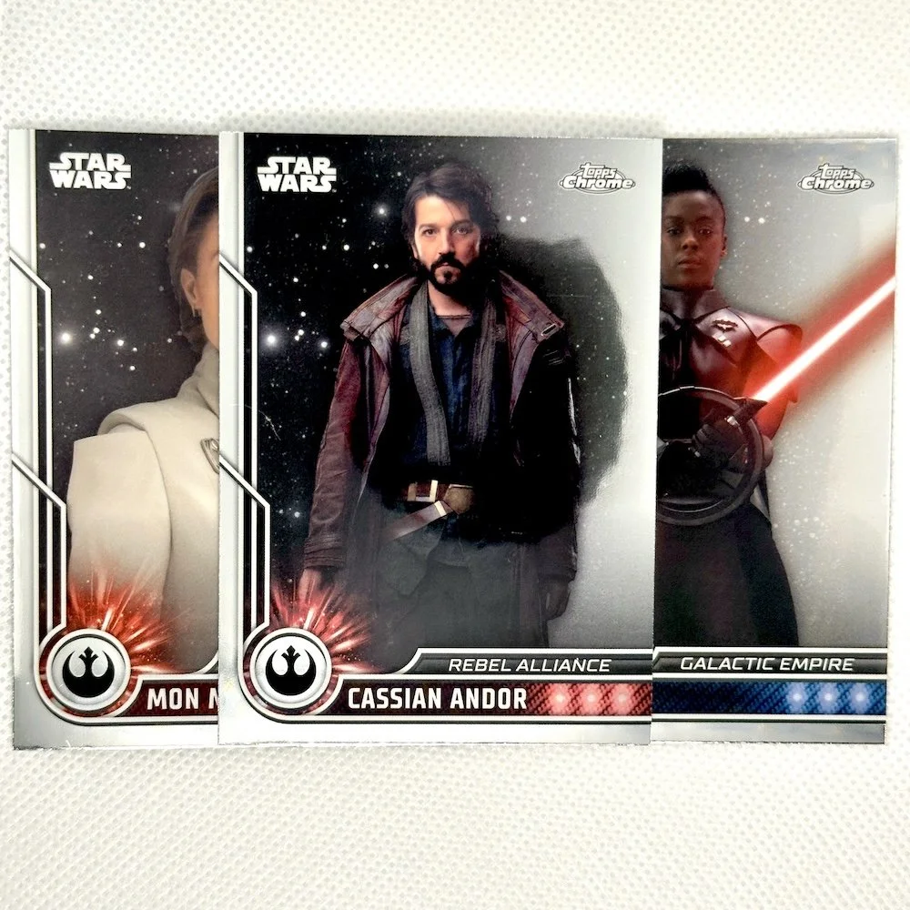 Three Star Wars character trading cards on a white surface, featuring Mon Mothma, Cassian Andor, and a character from Galactic Empire, with space backgrounds.