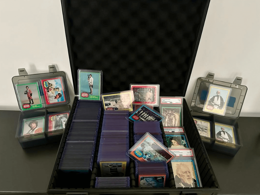 A collection of trading cards organized in a black plastic case with card sleeves and small plastic boxes on a black surface.