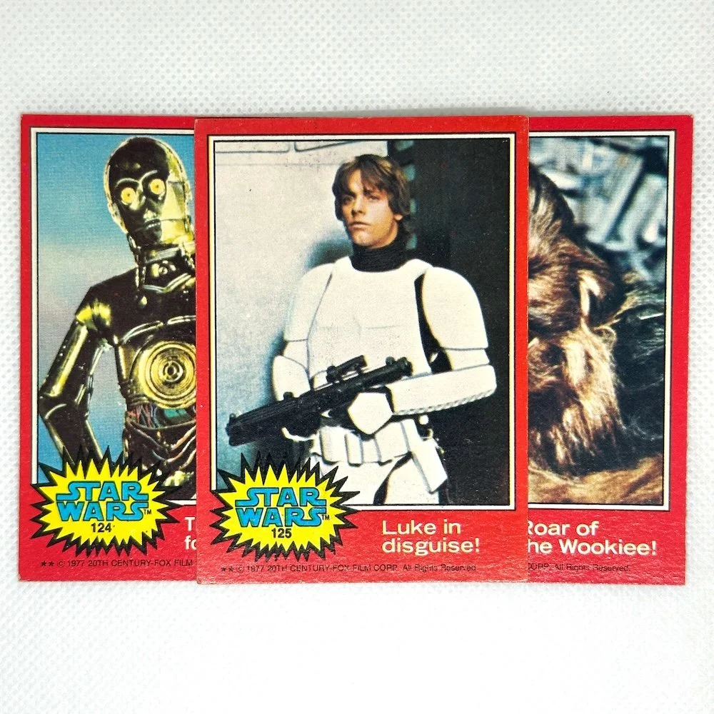 Three vintage Star Wars trading cards featuring characters from the original movies, including C-3PO, Luke Skywalker in Stormtrooper armor, and Chewbacca.