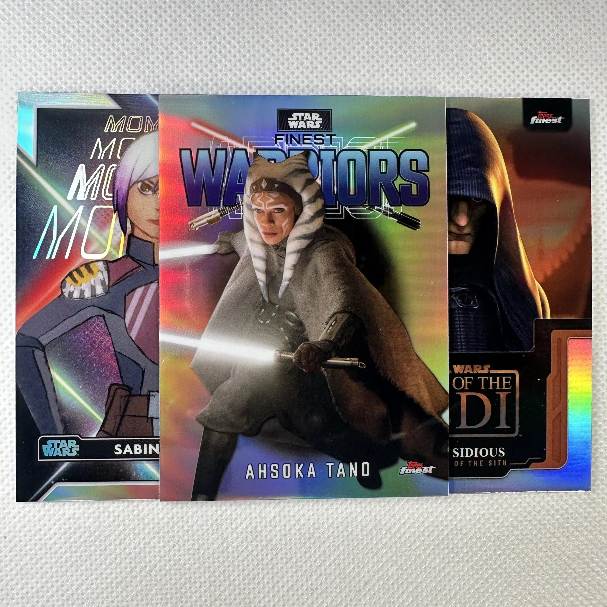 Three Star Wars trading cards featuring characters Sabine Wren, Ahsoka Tano, and Sidious from the Disney series, with colorful backgrounds and holographic designs.