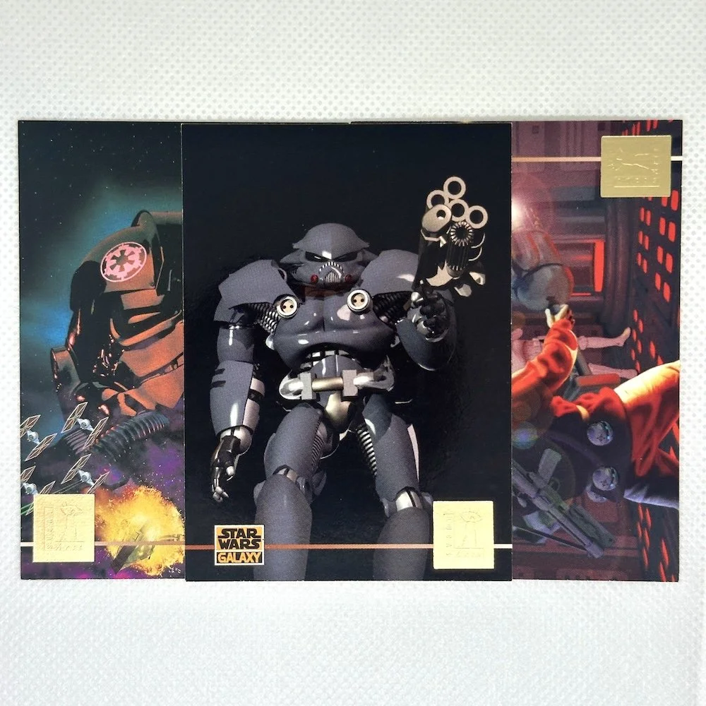 A large Star Wars robot toy with a black and gray body, holding a gun, displayed on a wall poster with Star Wars graphics.