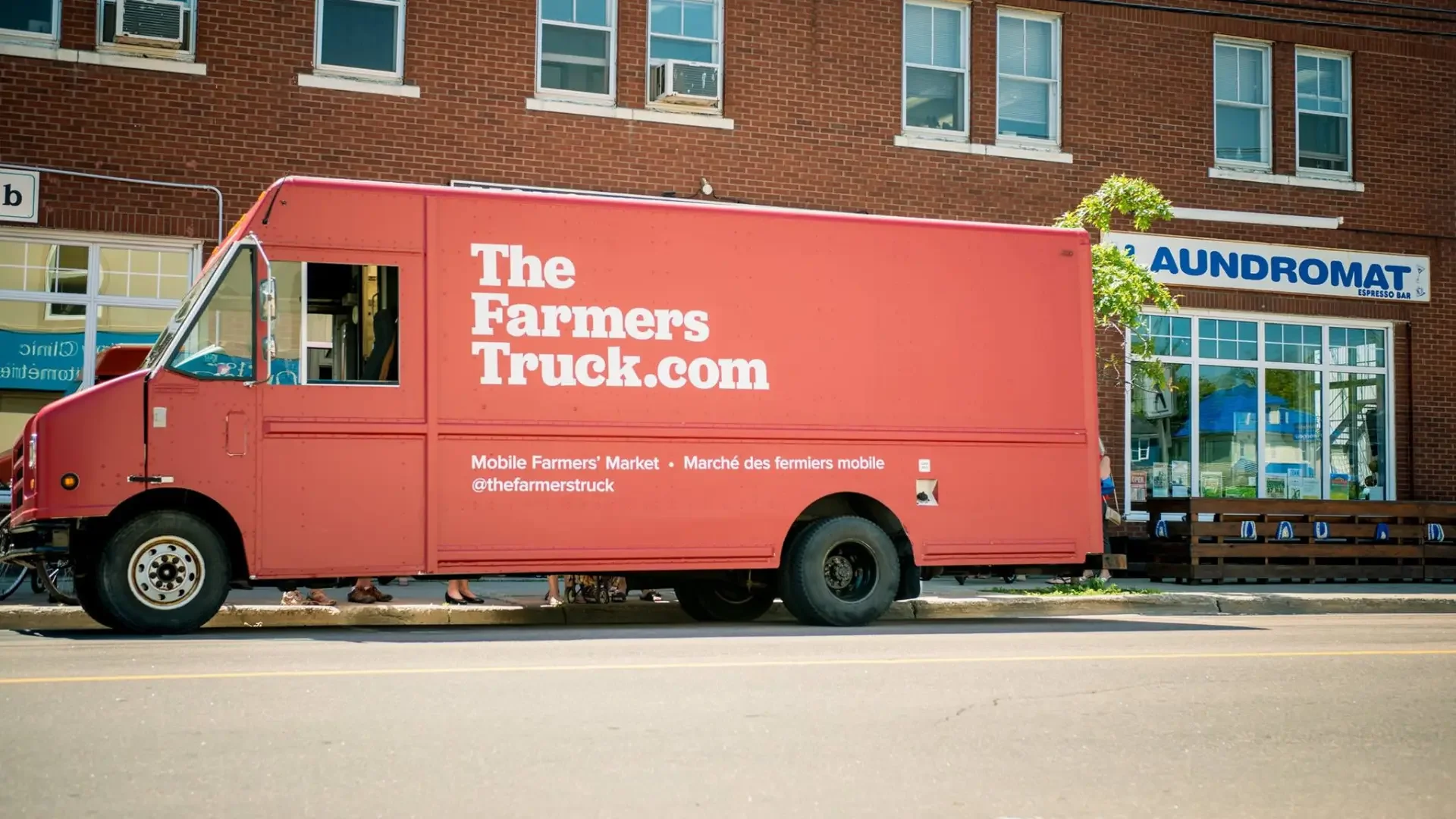 A red mobile market truck parked with the farmer'struck.com website along the side