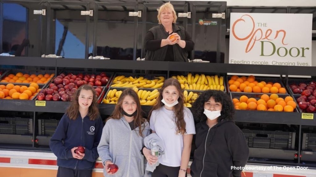 Students pose in front of a mobile market holding produce
