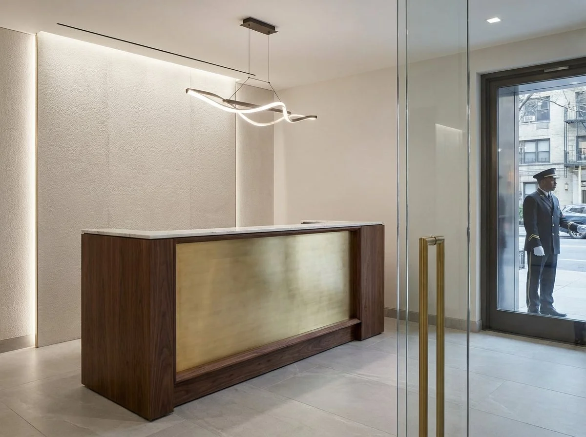 Renovated NYC building entryway and reception area with large windows, exposed brick, and custom pendant lighting