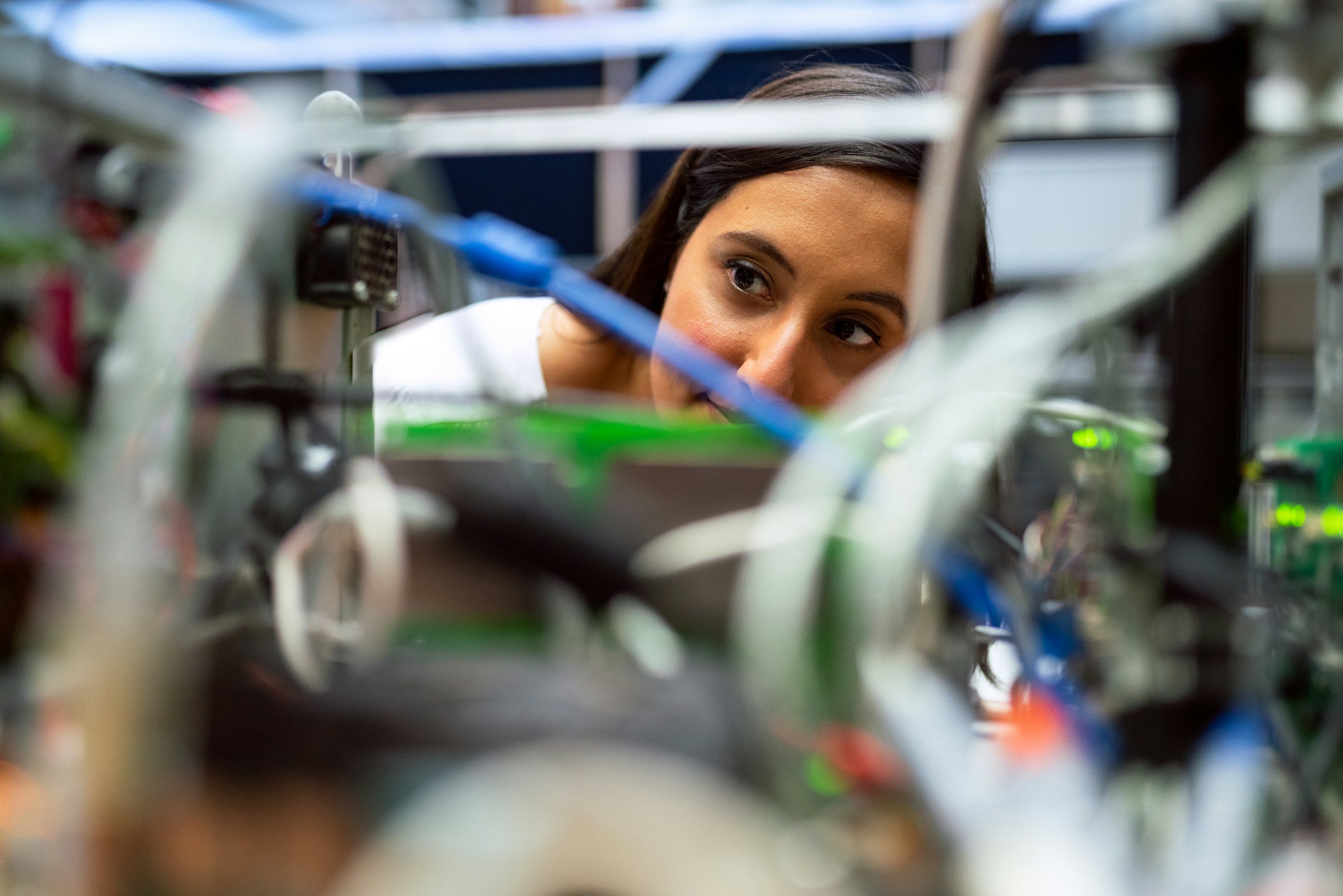 A woman looks through electronic equipment with wiring and circuit boards in the foreground.