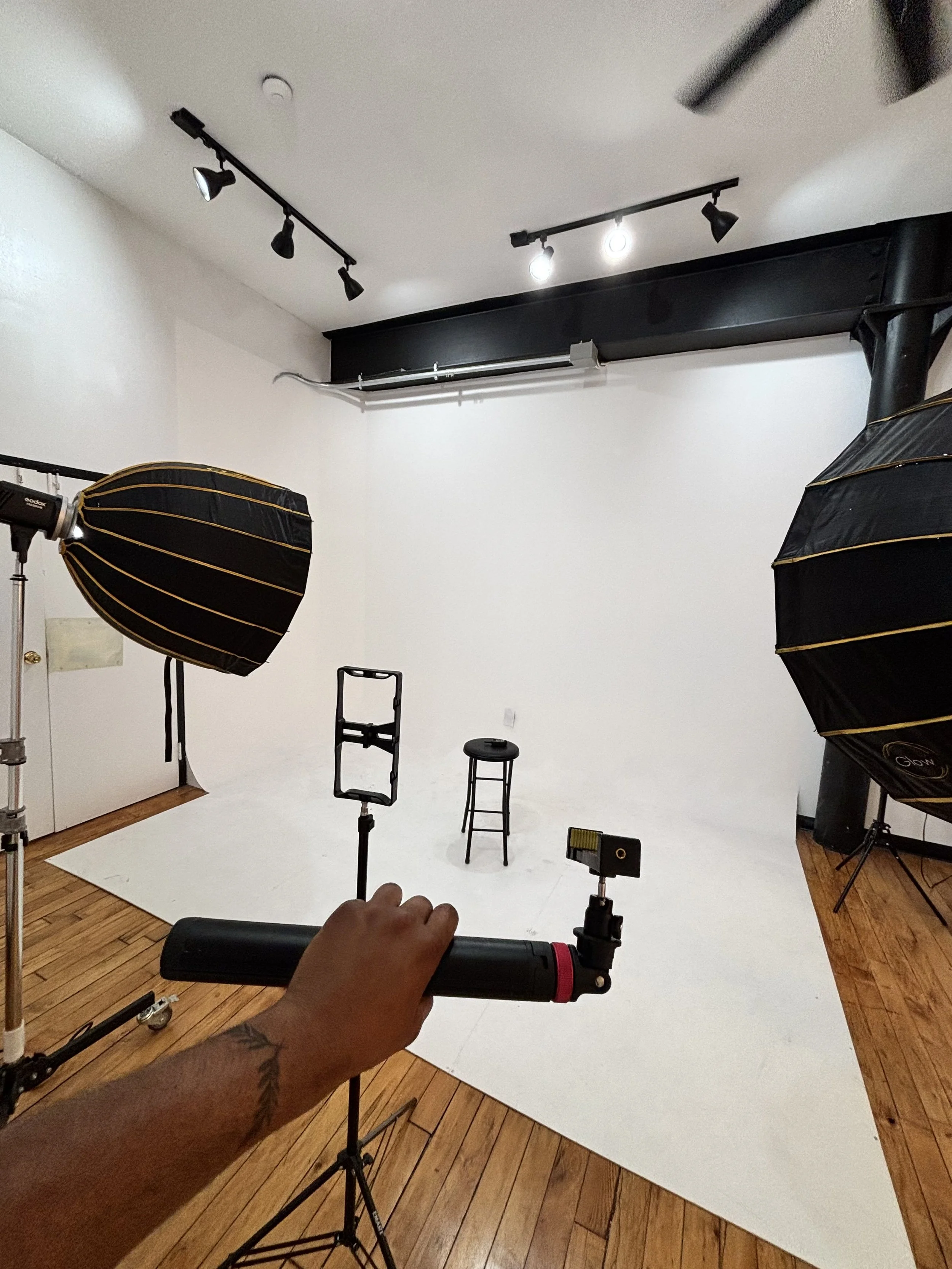Photography studio with black and gold softbox lights, a white backdrop, a stool, a small black table, and various lighting and camera equipment.