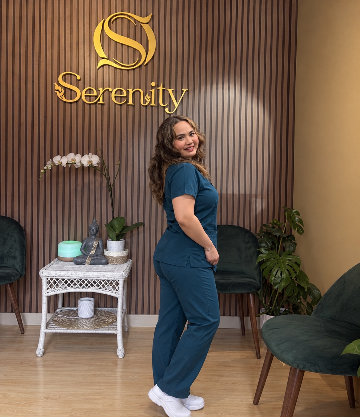 Professional female massage therapist in grey uniform sitting in a warm Thai spa room with candles and plants, representing Serenity Thai Wellness & Massage in Los Angeles.