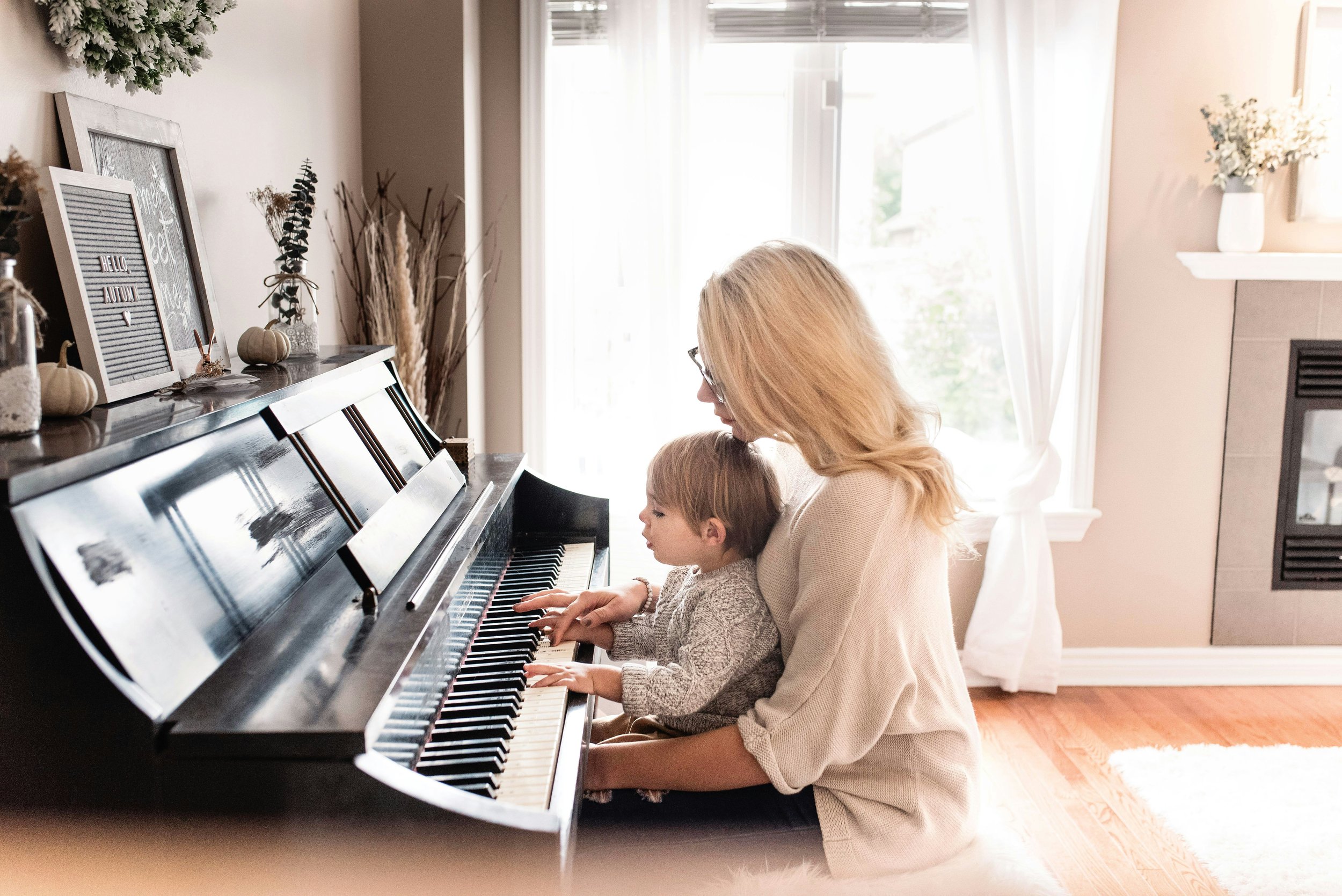 Piano teacher with small child in her lap sitting at the piano learning music.