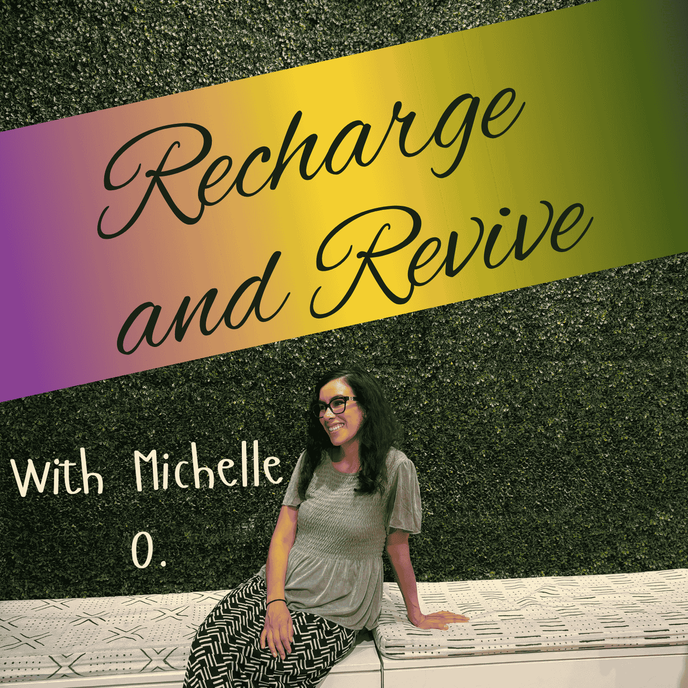 A woman with glasses and long dark hair sitting on a bench in front of a black hedge wall with a colorful sign that reads 'Recharge and Revive with Michelle.'
