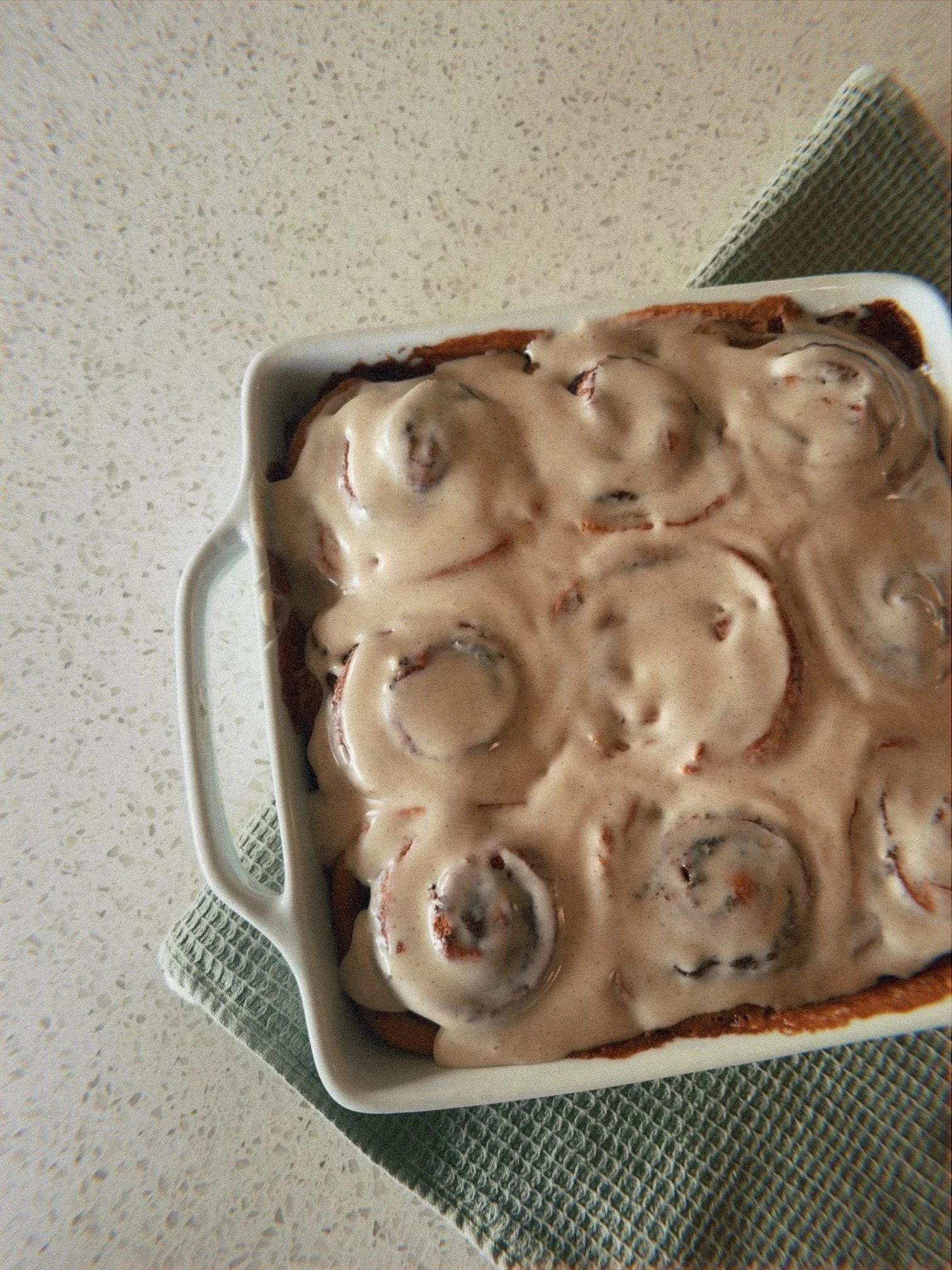 A baking dish filled with cinnamon rolls topped with cream cheese frosting.