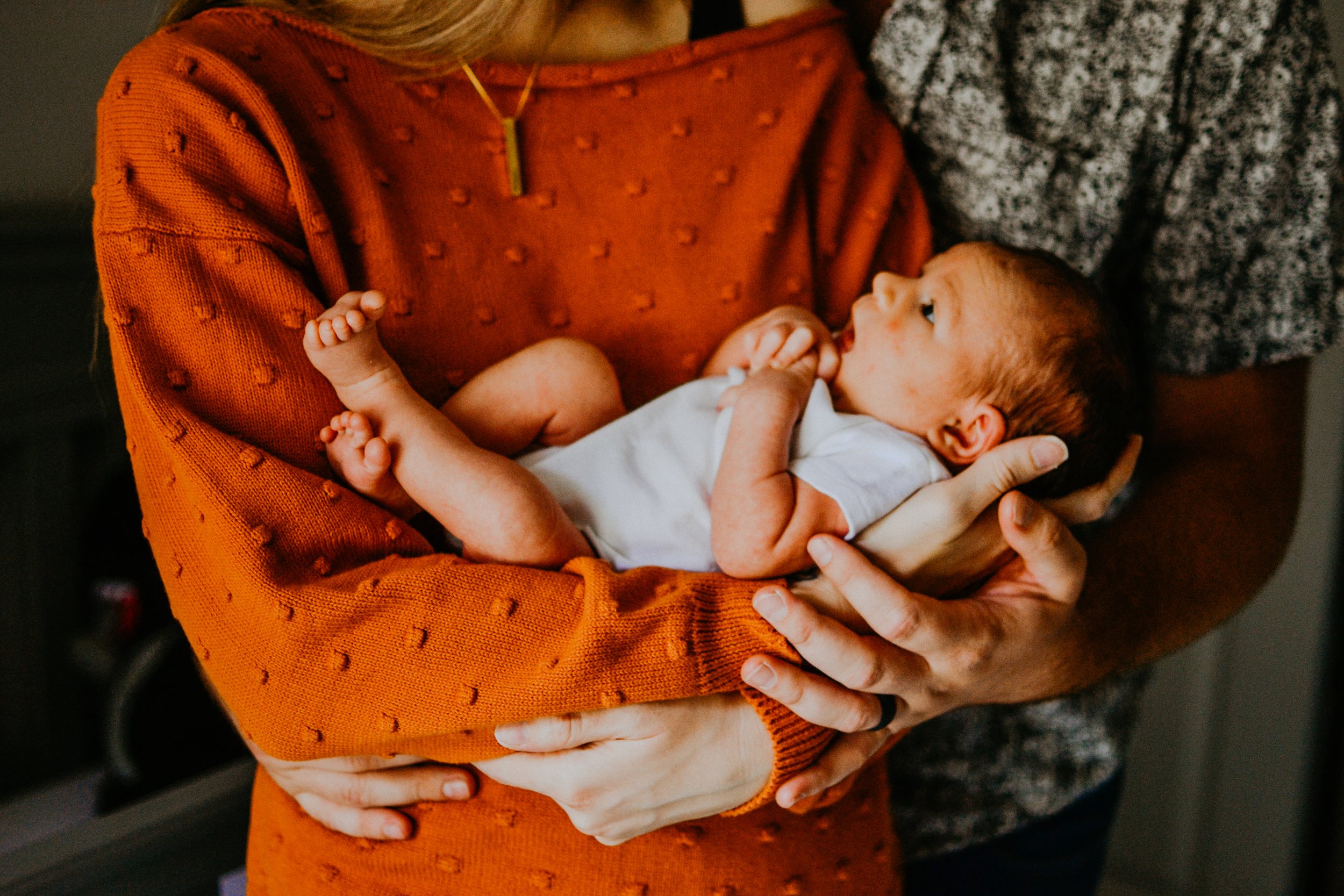 A mother in an orange sweater holding a newborn baby in their arms.