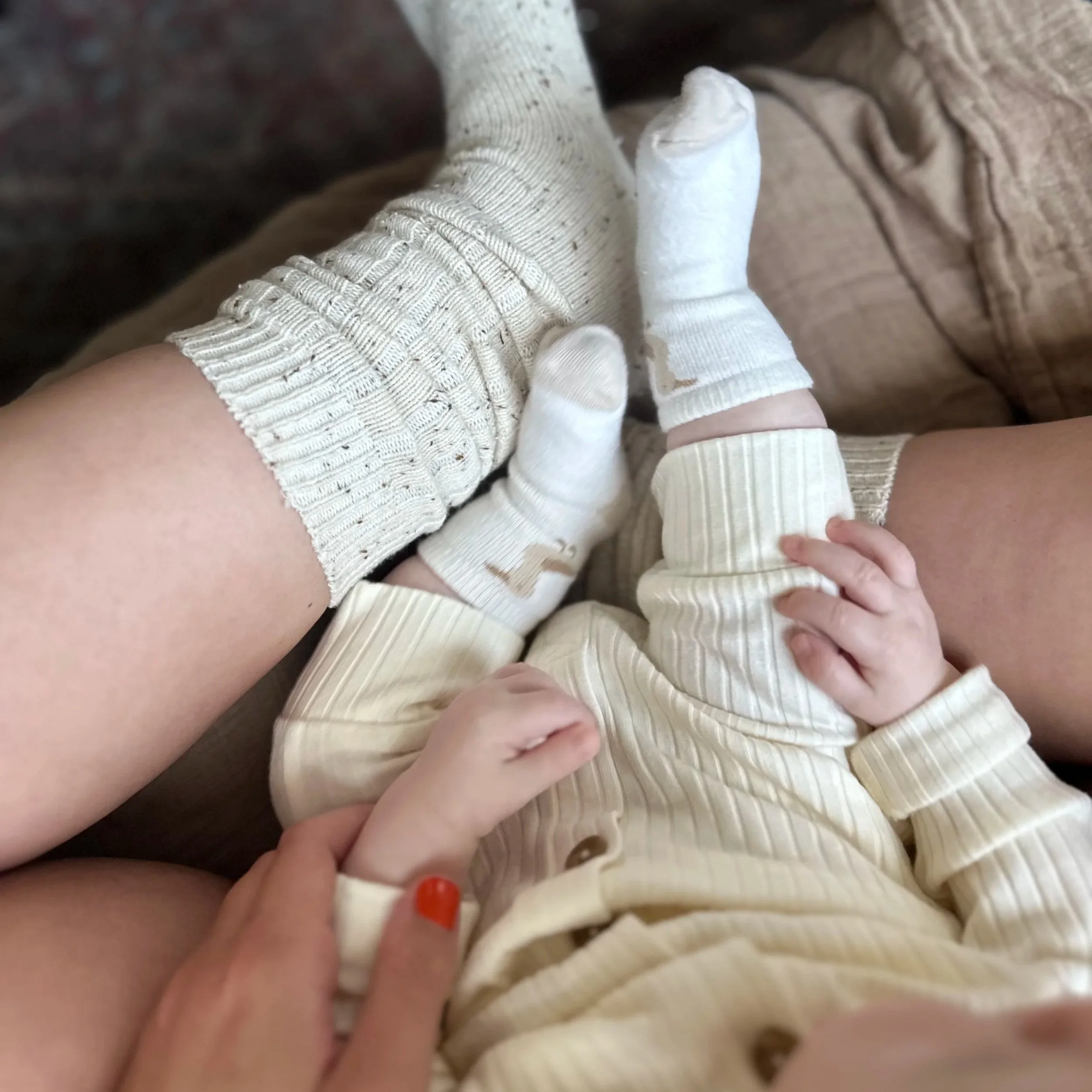 Close-up of a young child and an adult holding each other's hands, both wearing cream-colored, striped pajamas and socks.