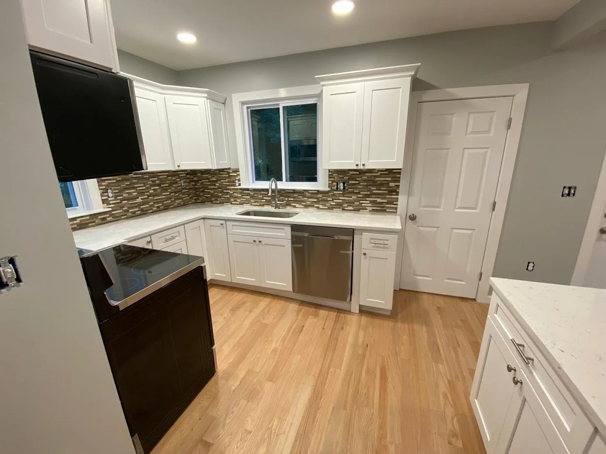 Kitchen with white cabinets, a mosaic tile backsplash, a window above the sink, a stainless steel dishwasher, and a black stove, hardwood flooring, and a closed white door.