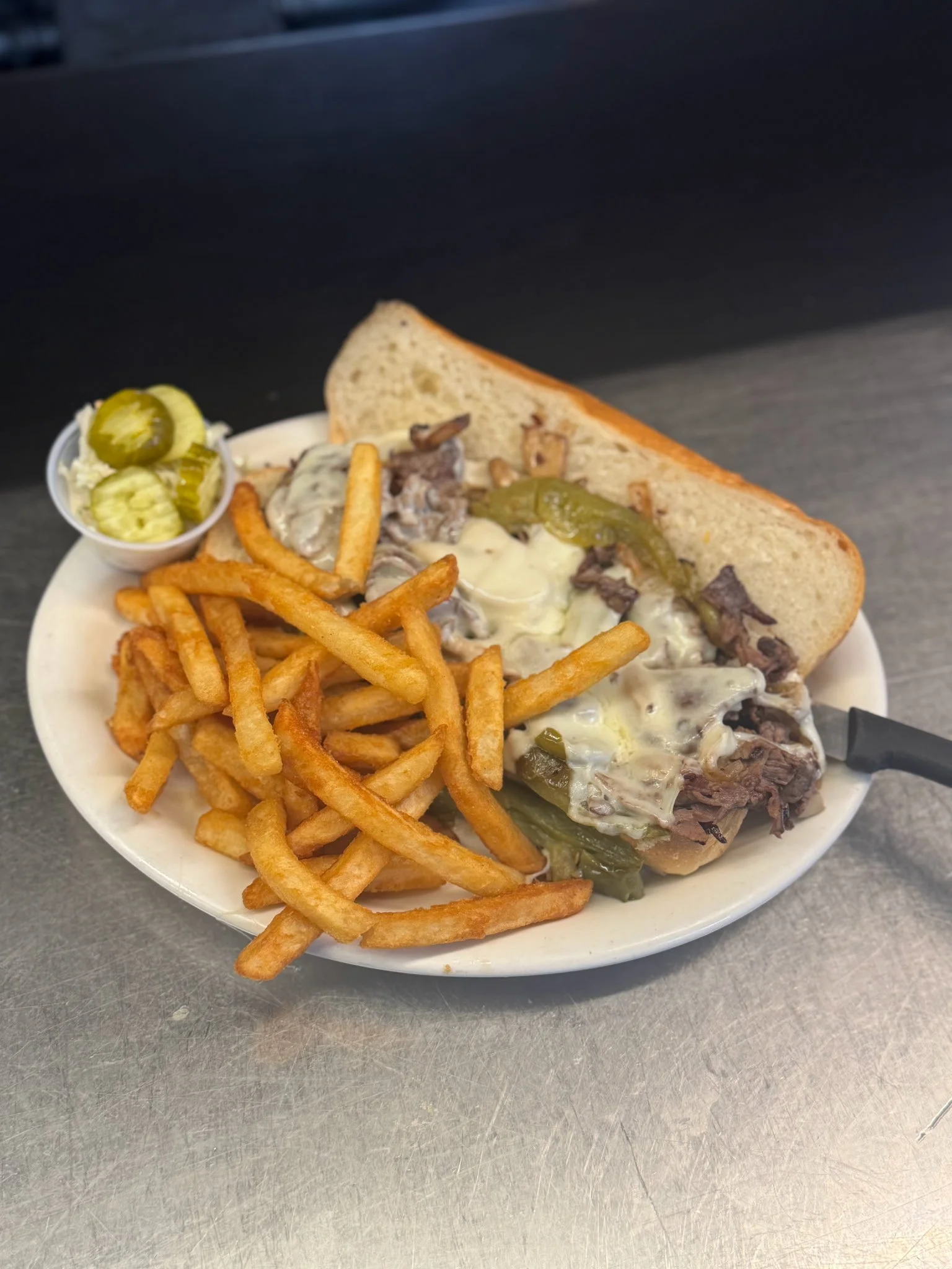 Plate with French fries, sliced pickles, beef sandwich with melted cheese and green peppers, and a slice of bread.