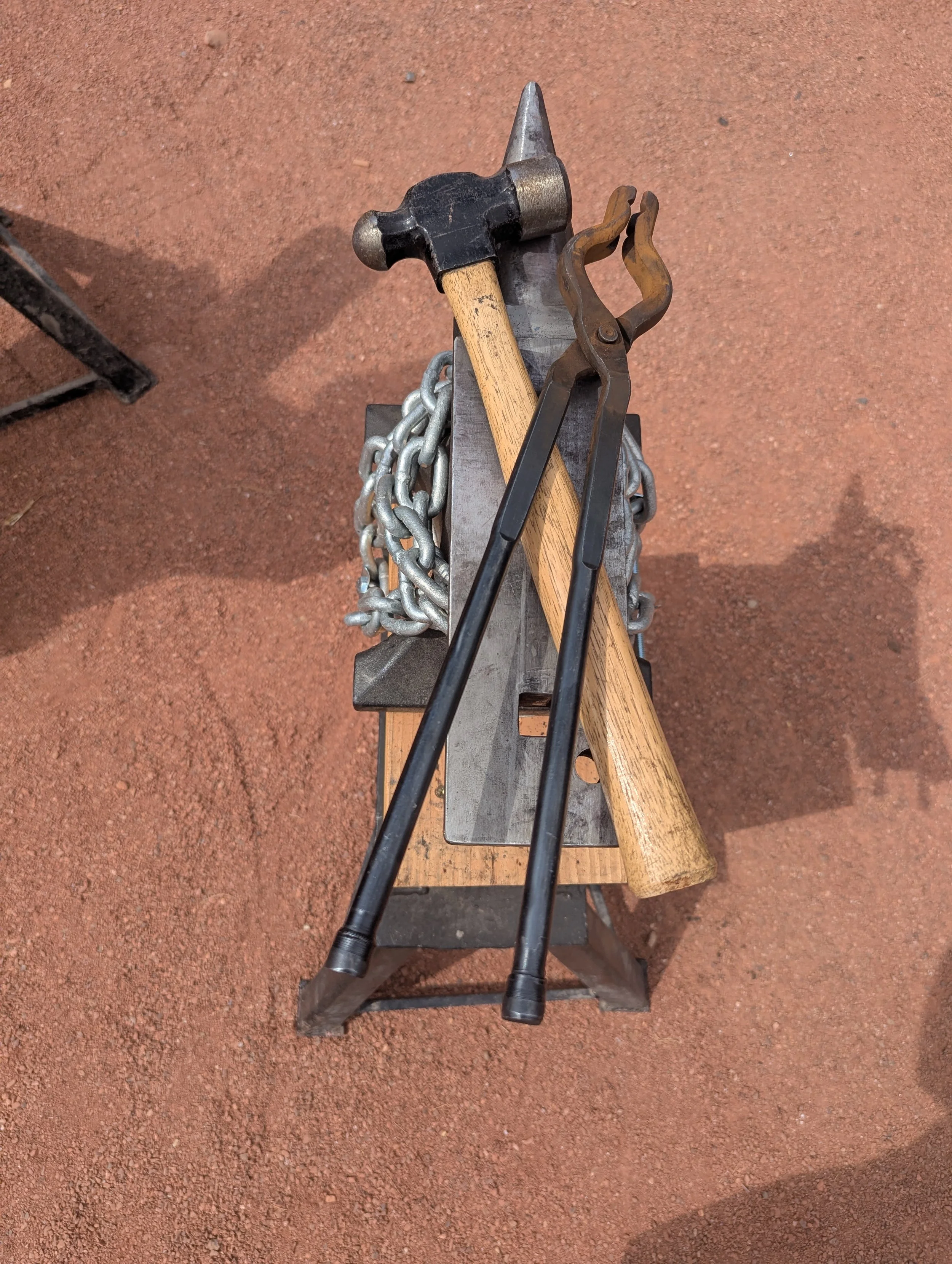 a set of blacksmith hammer and tongs crossed and laid over the top of an anvil.