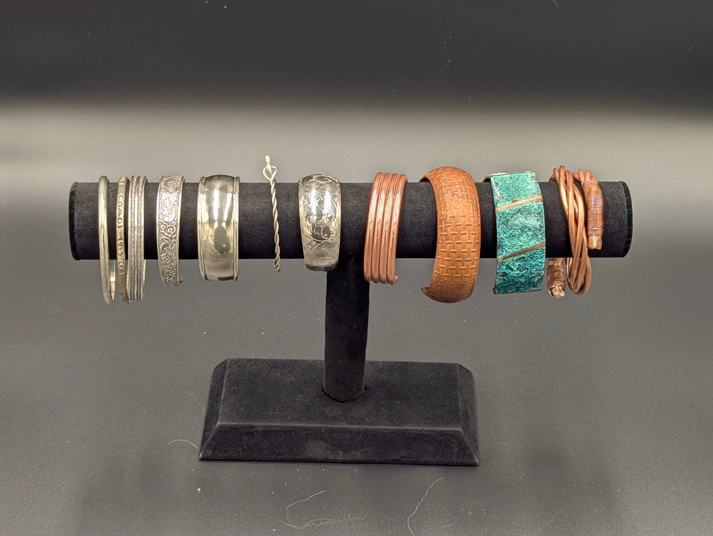 A collection of sterling silver and copper bracelets, bangles, and cuffs arranged on a black velvet display stand.