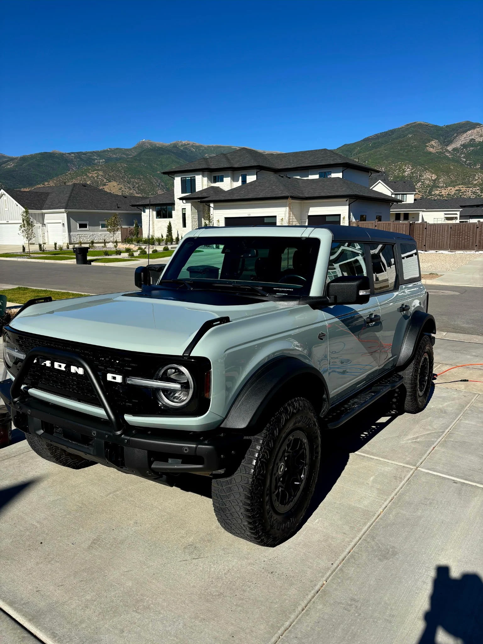 A white and black Ford Bronco SUV parked on a residential driveway with mountains in the background.