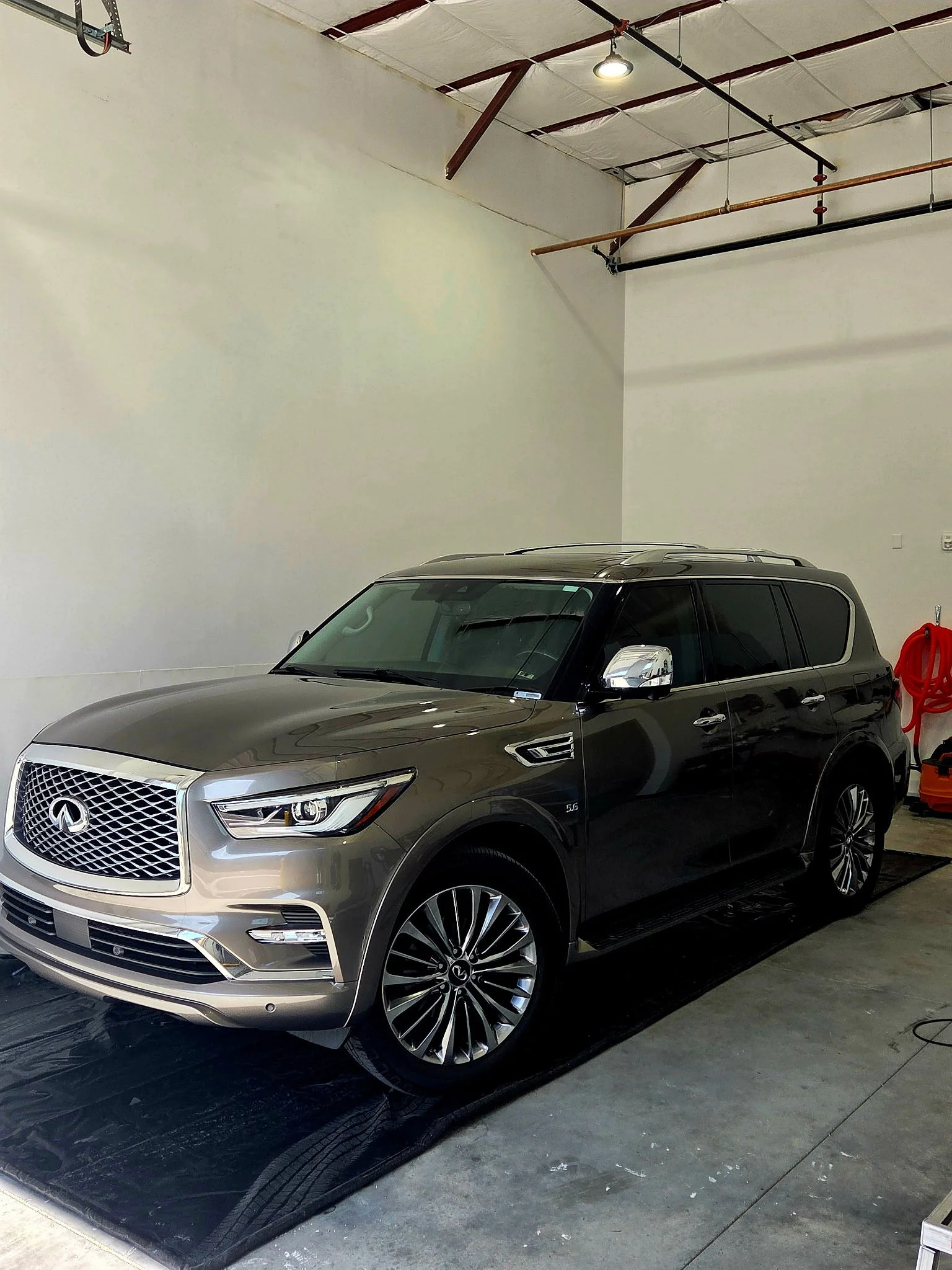 A gray Infiniti SUV parked inside a clean, white-walled garage with a red and black vacuum cleaner to the right.