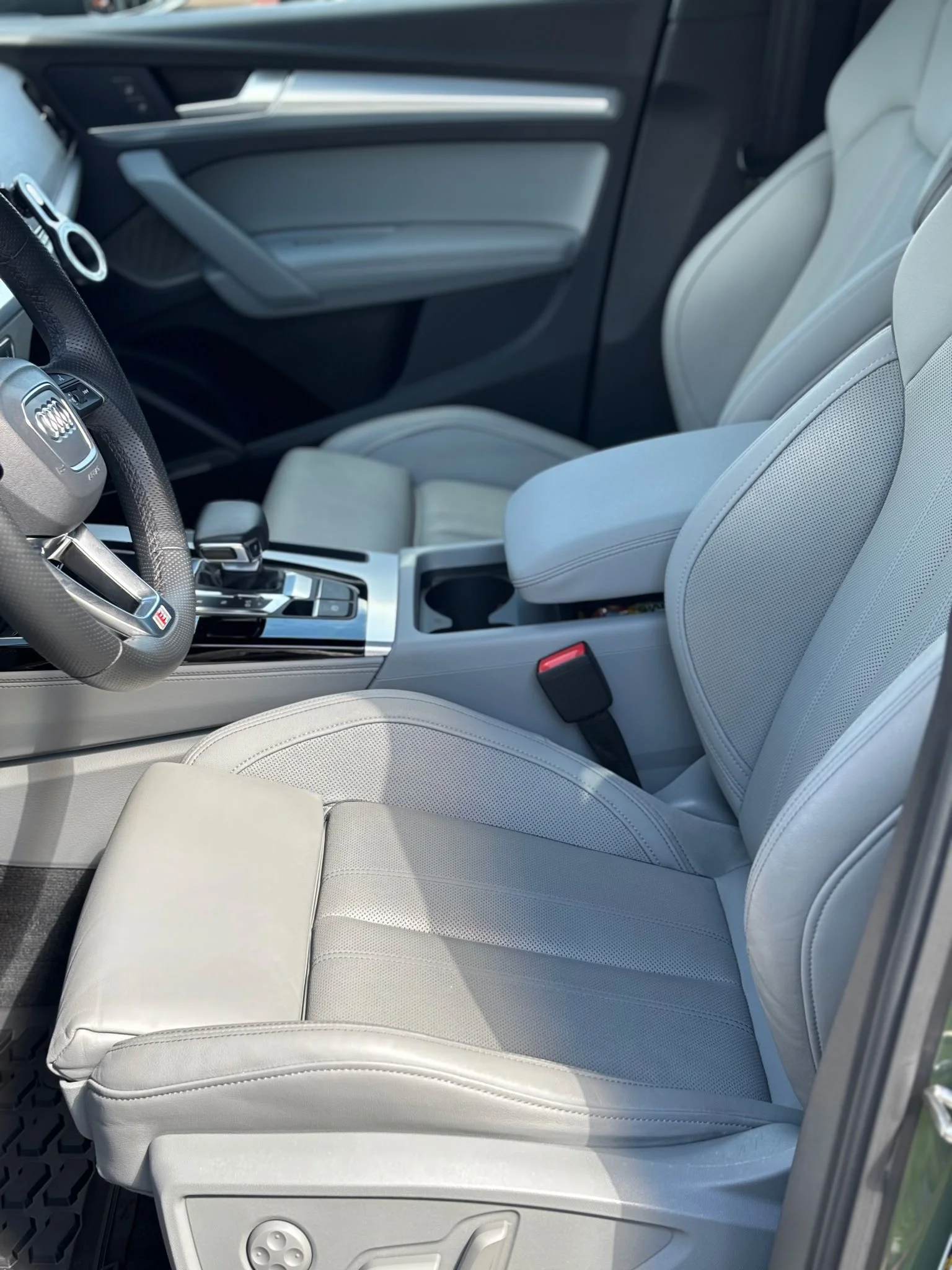 Inside the front seats of a light-colored car with light gray leather seats, a gear shifter, and a door panel.