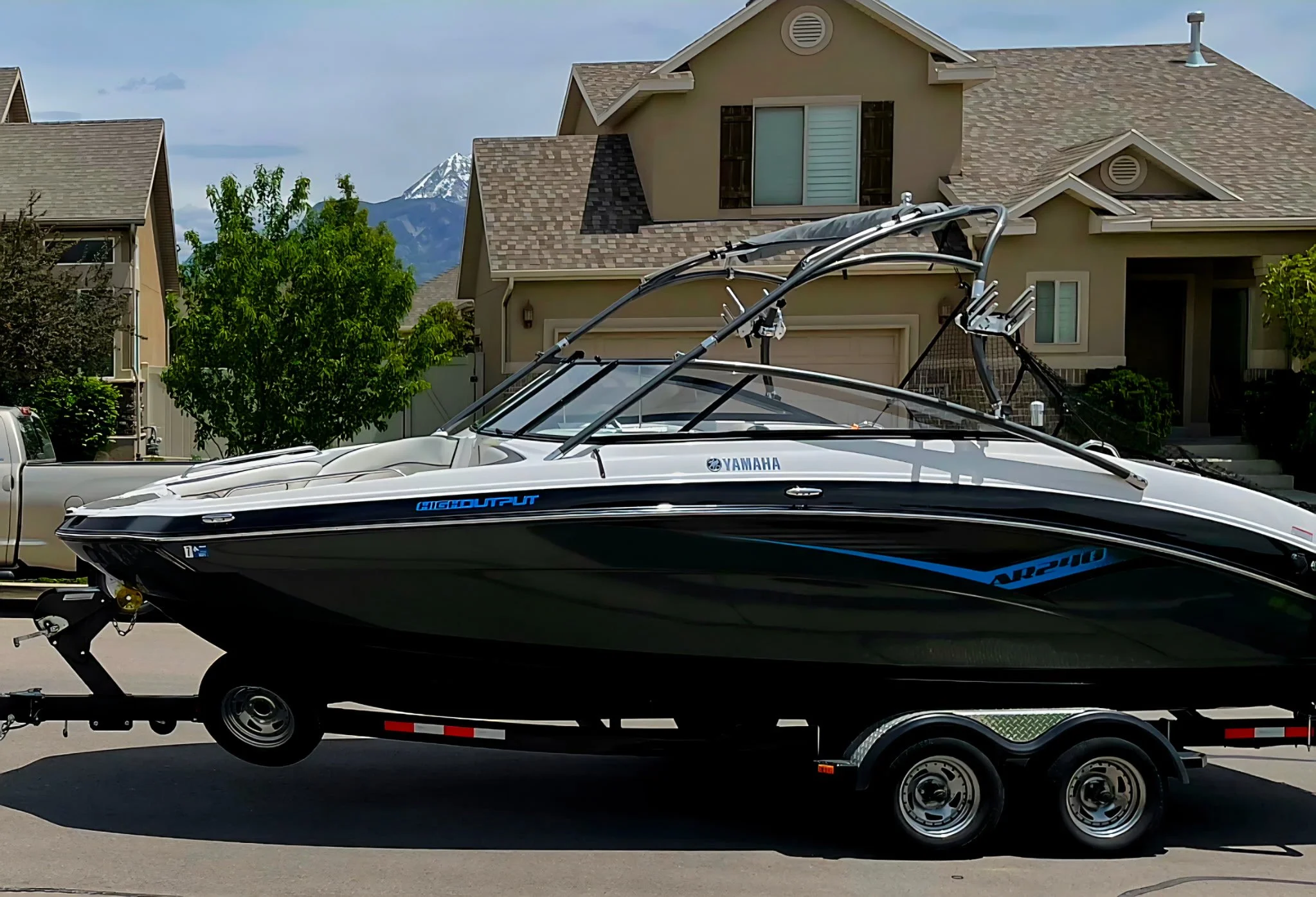A Yamaha AR210 high-output boat on a black double-axle trailer parked on a residential street with houses and mountains in the background.