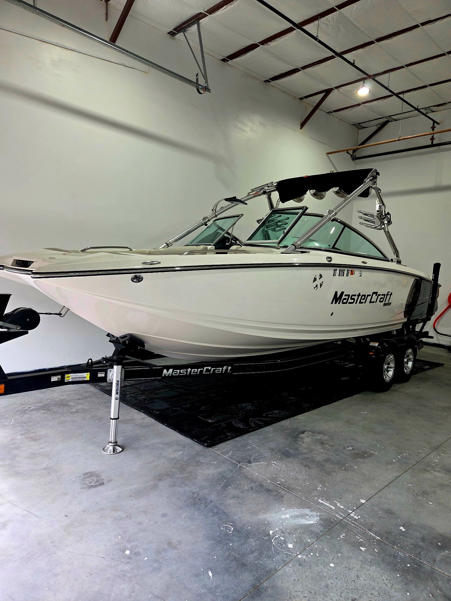 A white MasterCraft motorboat parked on a black trailer inside a storage or showroom facility.