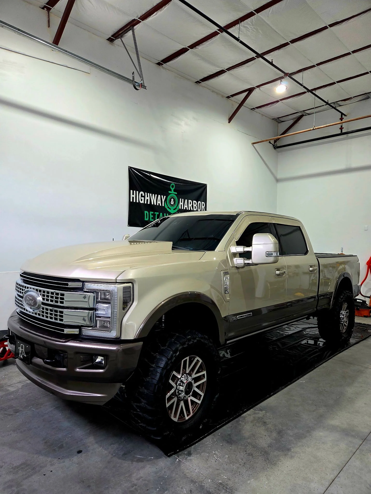 A beige and black Ford F-150 pickup truck parked inside an industrial-style garage with white walls and a high ceiling.