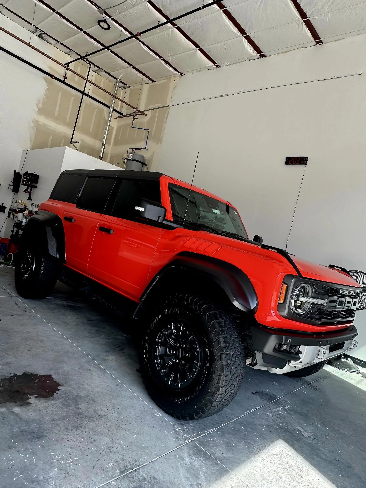 Red and black off-road vehicle inside a garage with an electronic clock on the wall showing 2:03.