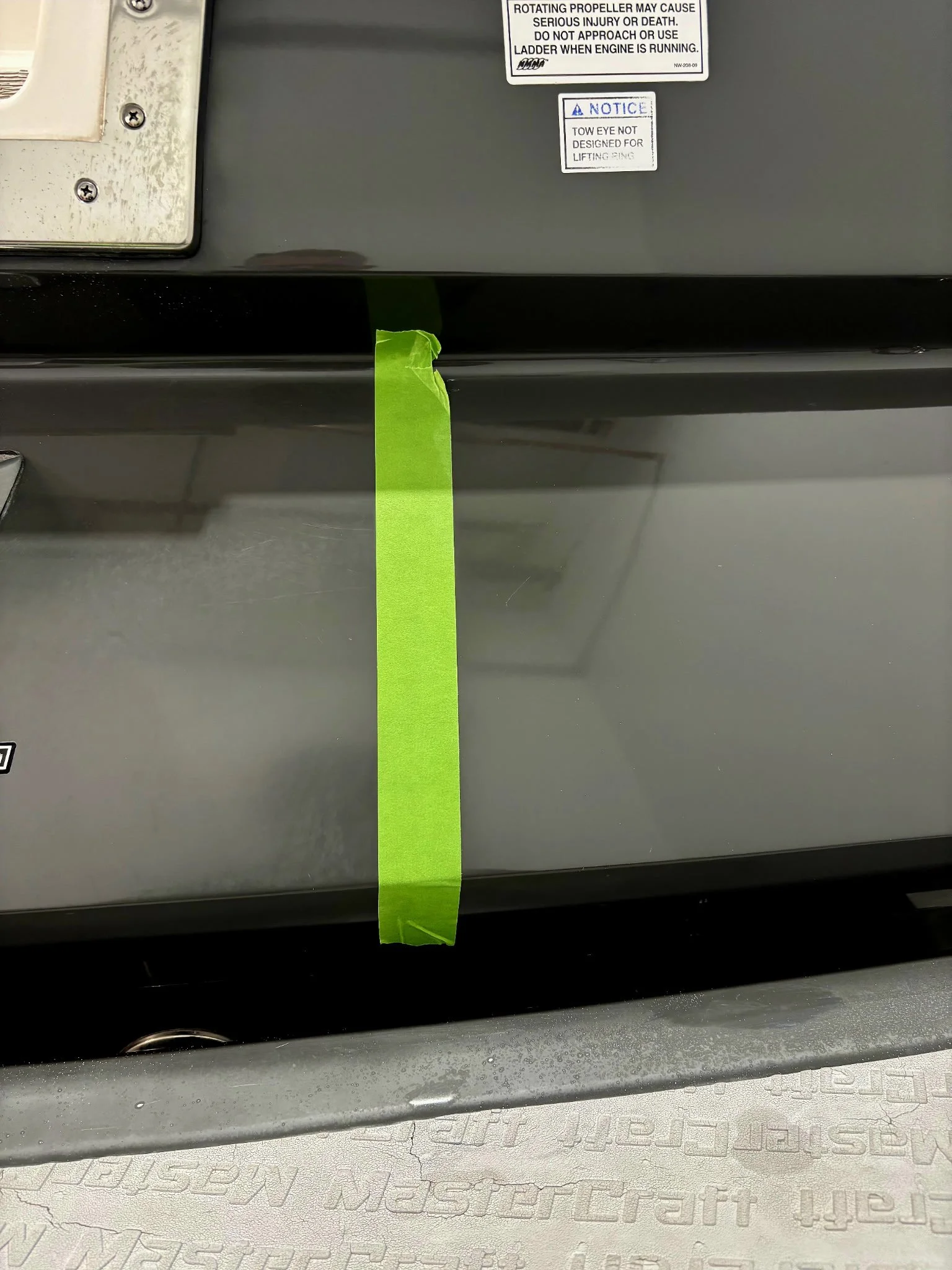 Close-up of a gray metal surface with green painter's tape and safety and warning labels on it.