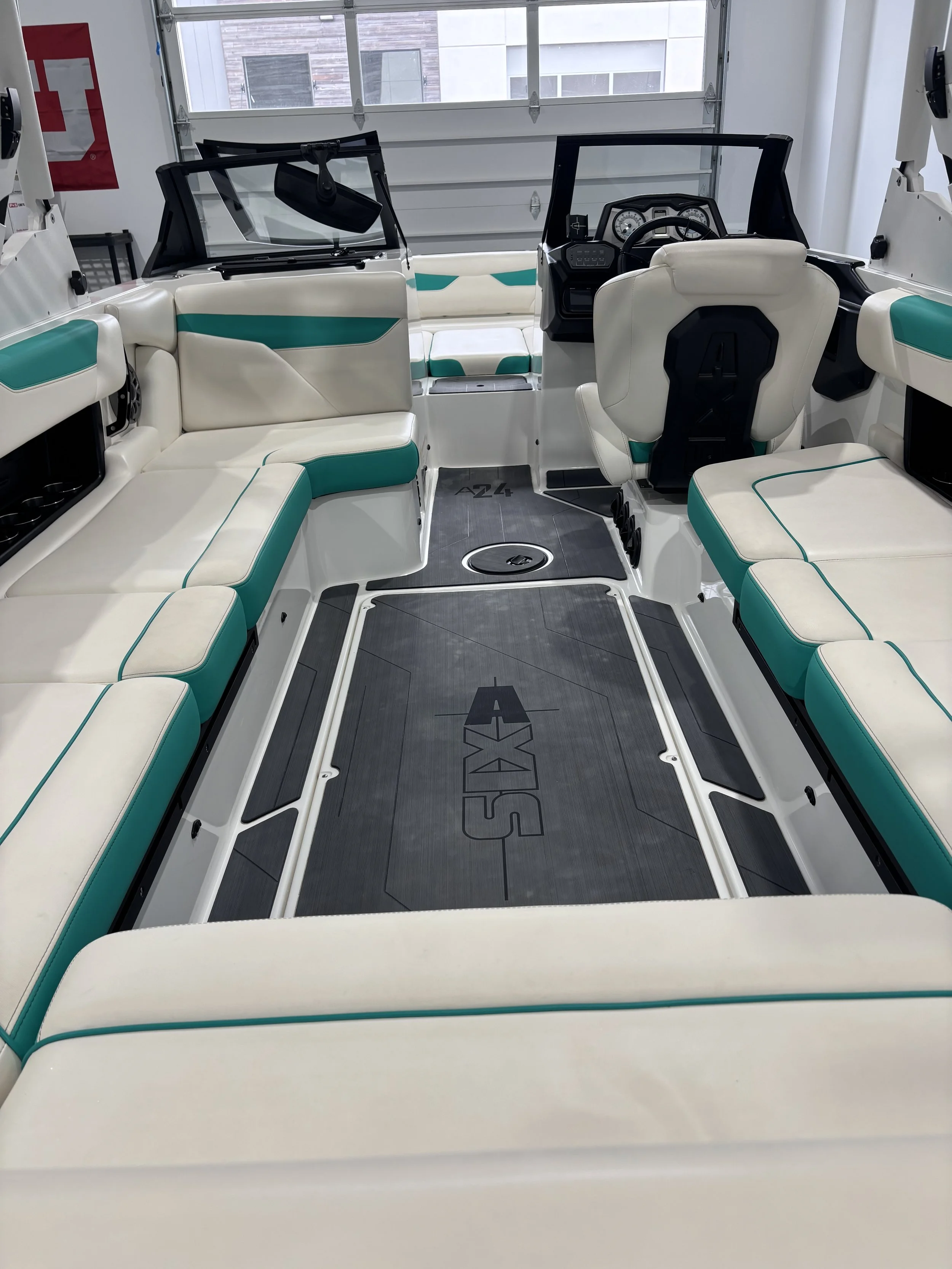 Interior of a boat with white and teal cushioned seats, steering wheel, and control panel, parked indoors in a garage.
