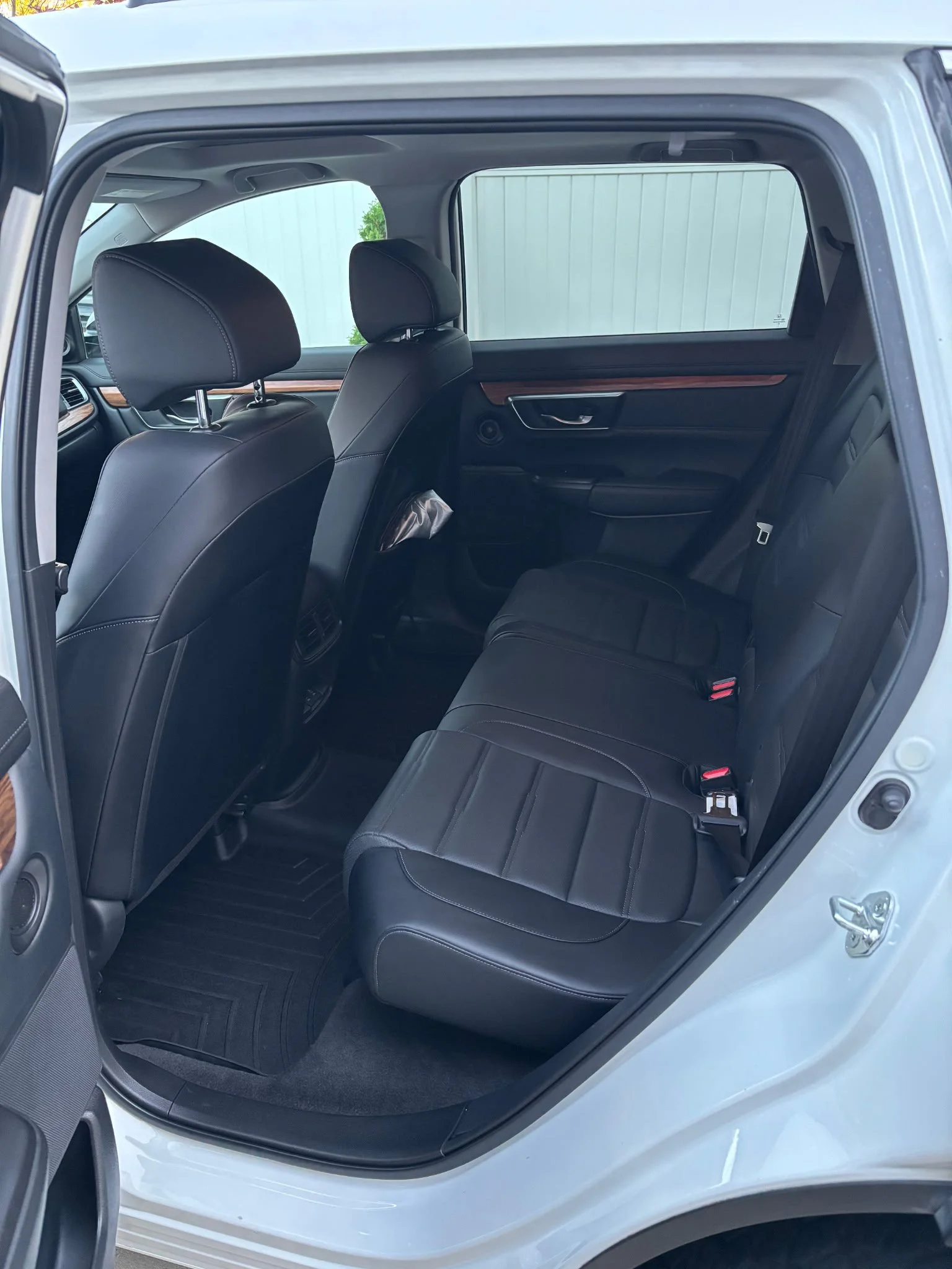 The interior rear seats of a white SUV with black leather seats and a wooden trim on the door panels.